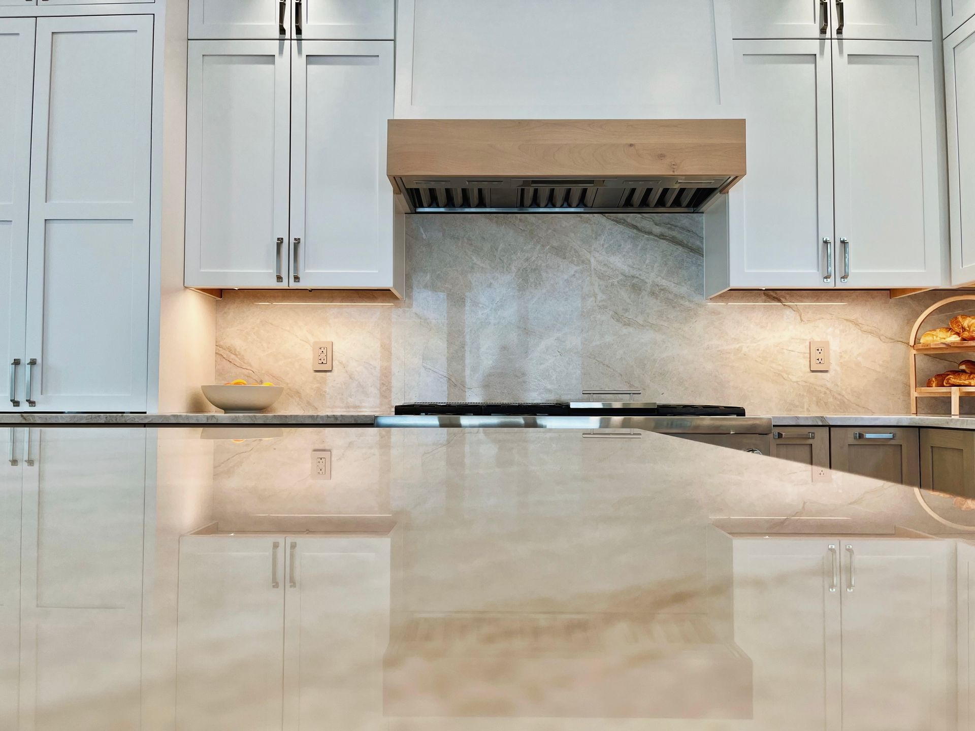 Modern kitchen with white cabinets, stainless range hood, and marble countertop reflection