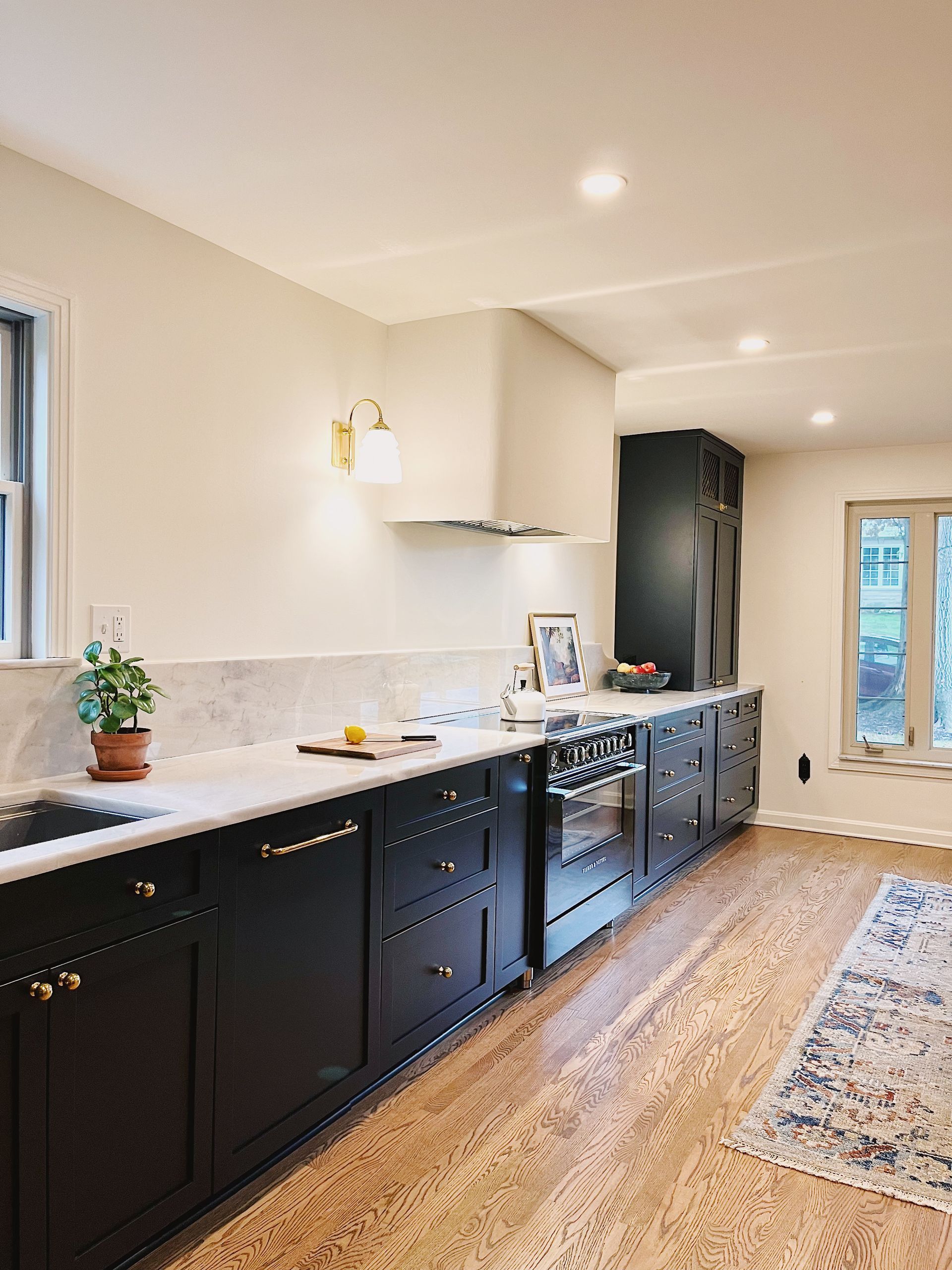 Long, narrow kitchen with black cabinets, white countertops, woven rug, and glass doors at the end