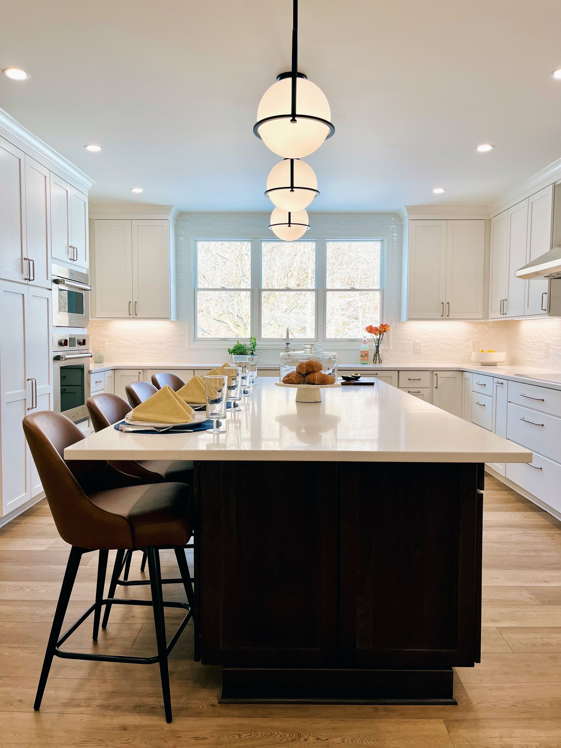 Bright modern kitchen with a large island, pendant lights, white cabinets, and a window over the sink.