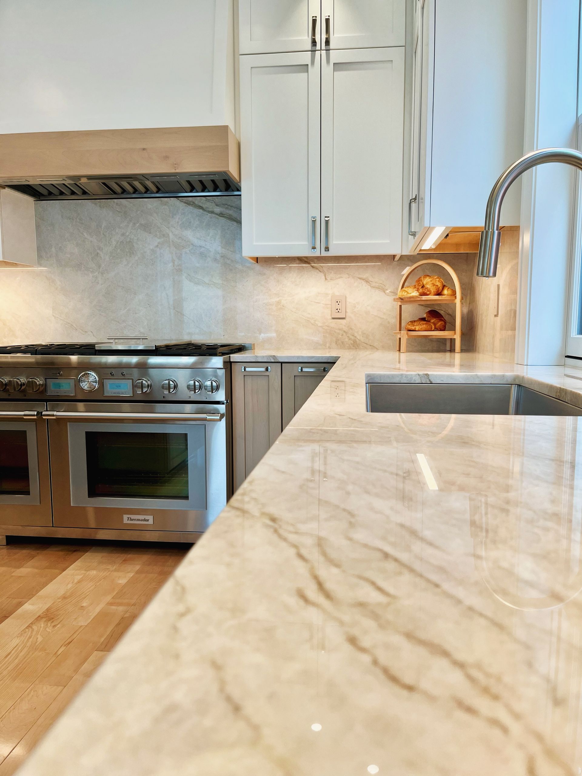 Modern kitchen with stainless steel range, white cabinets, marble island, and window over sink
