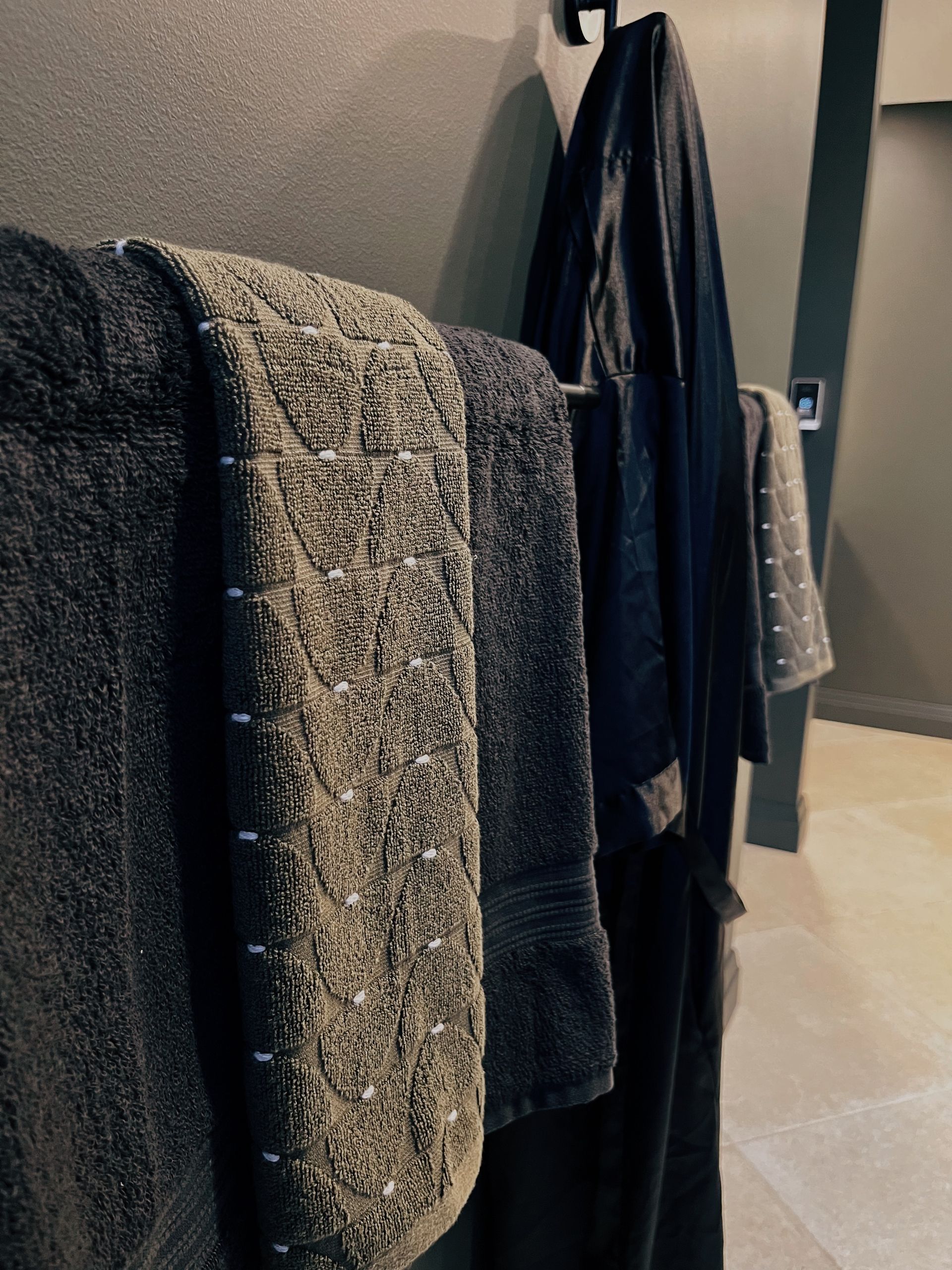 Coats and towels hanging on a wall rack in a hallway, with a textured gray towel in front.