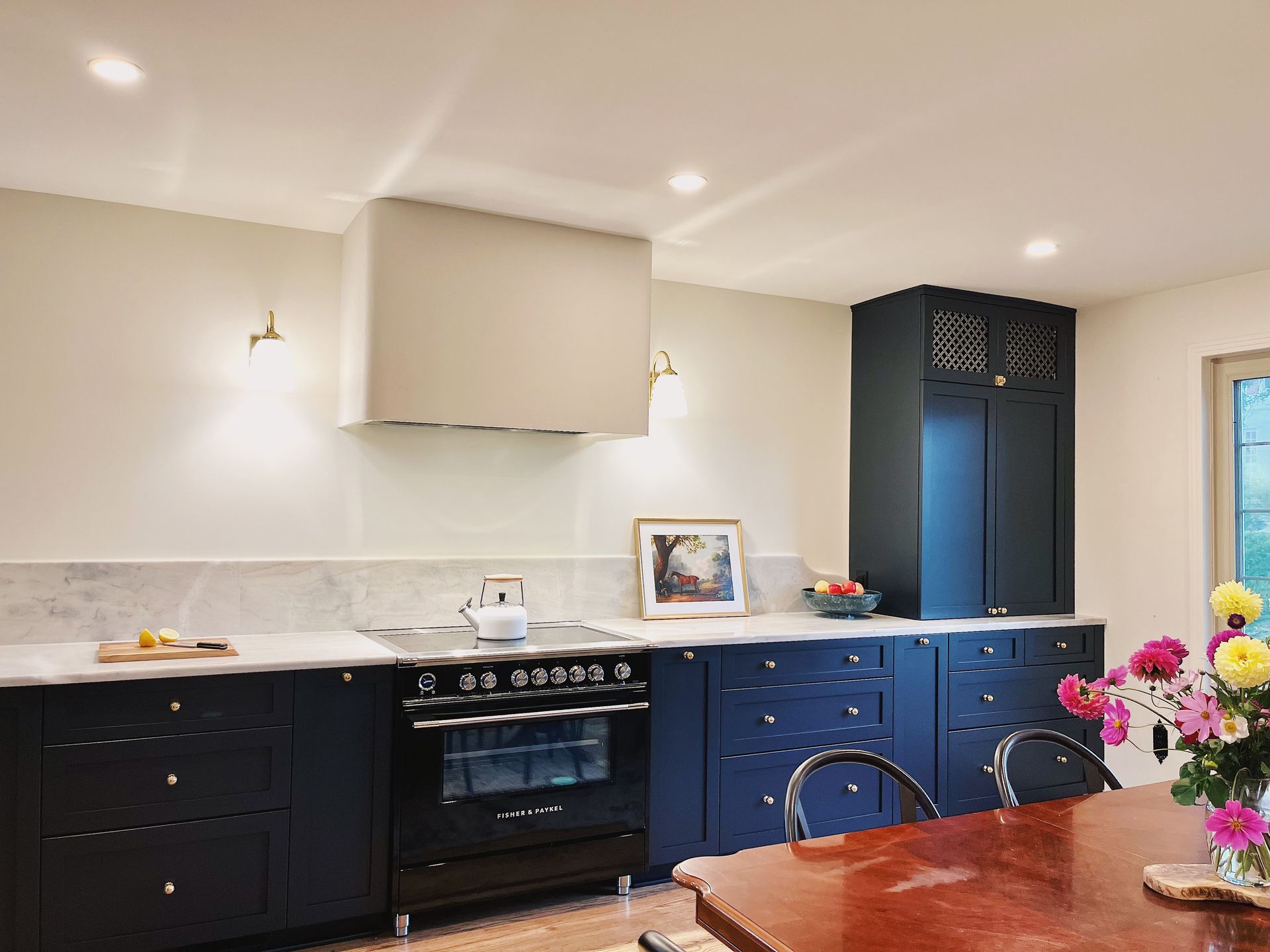 Modern kitchen with dark cabinets, marble counters, blue island, stove, and flowers on a wooden table
