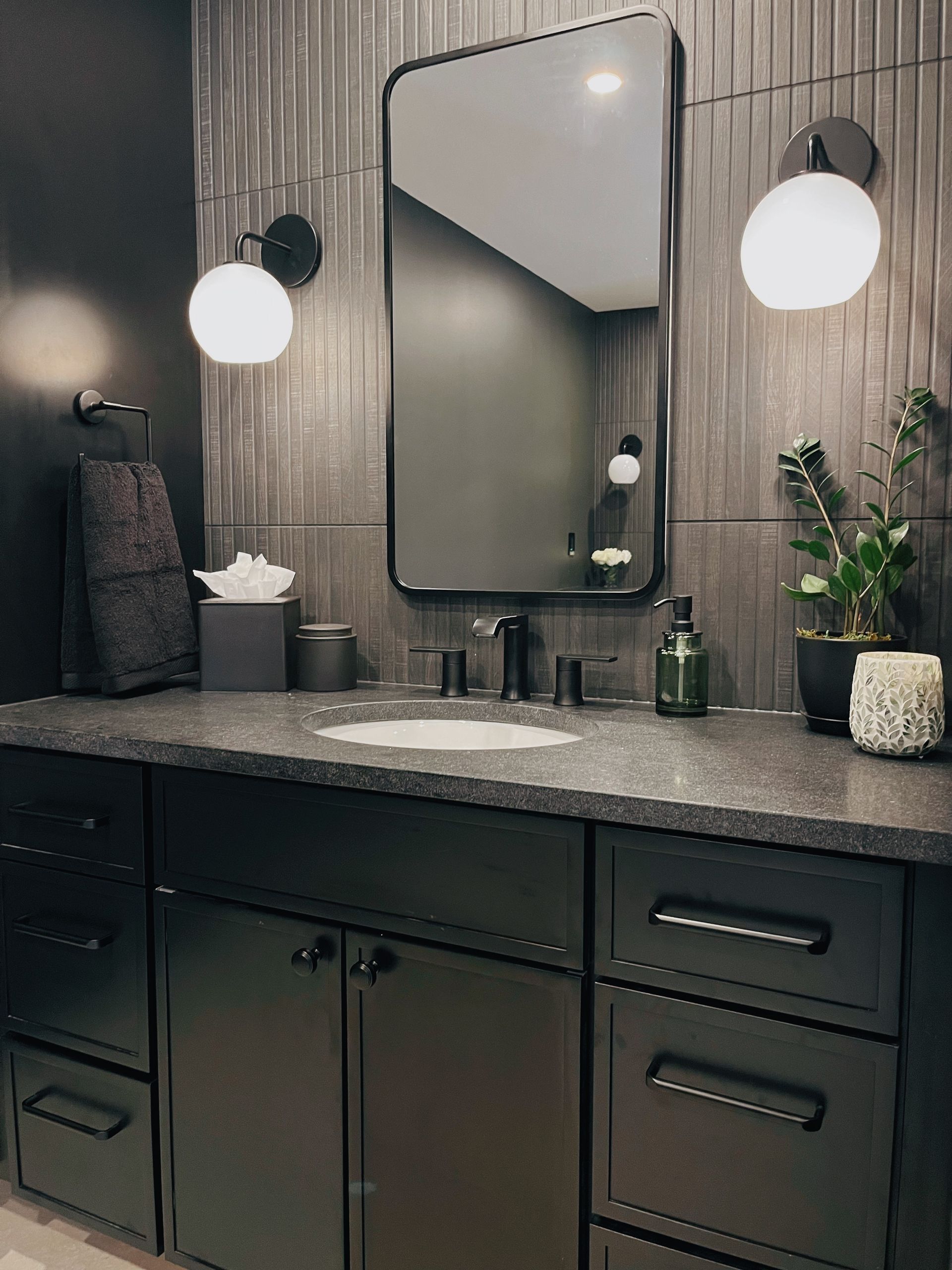 Modern dark bathroom vanity with double sinks, round sconces, mirror, and decorative plants