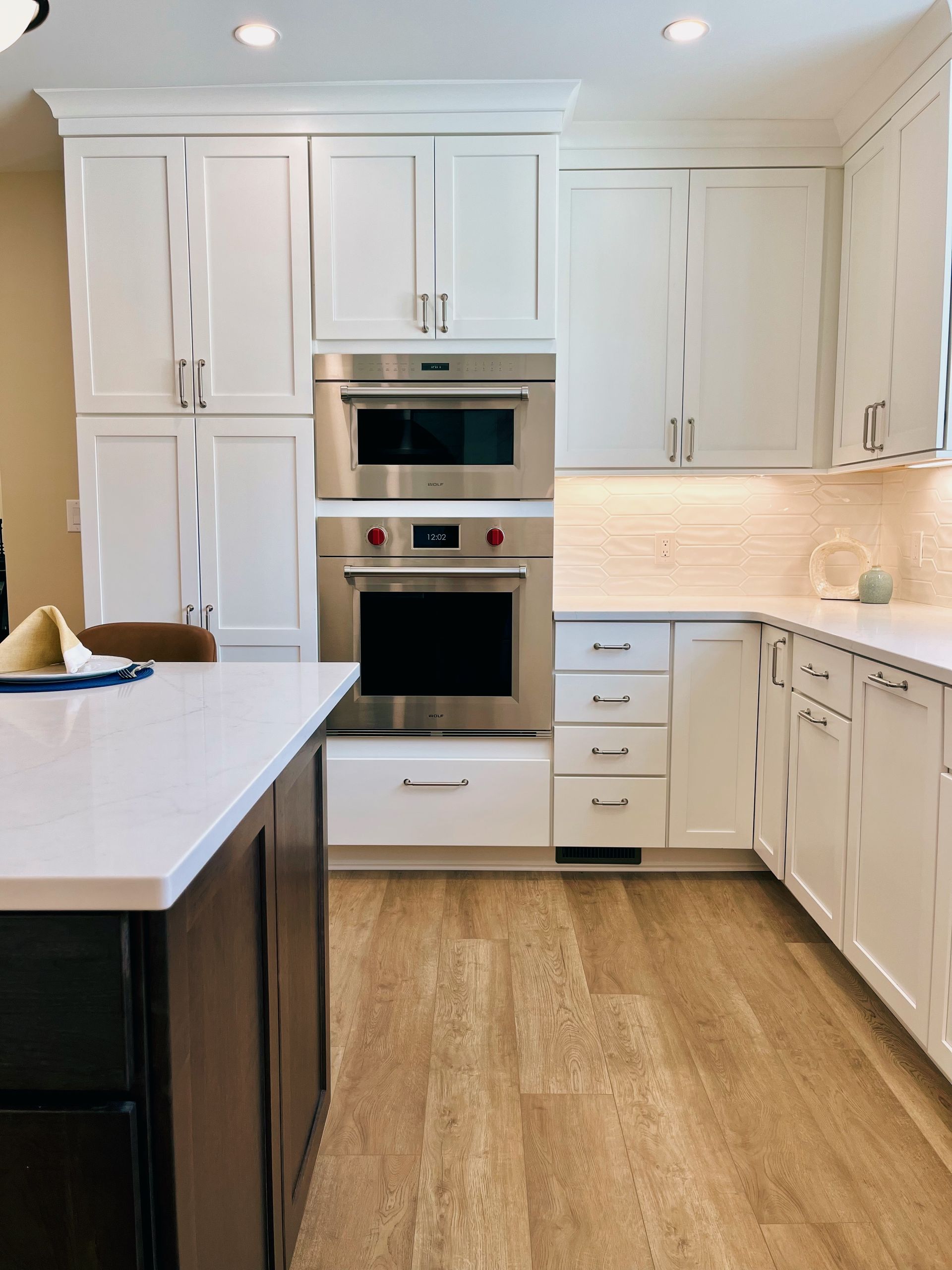 Bright white kitchen with built-in oven, white cabinets, and a large island over wood flooring.