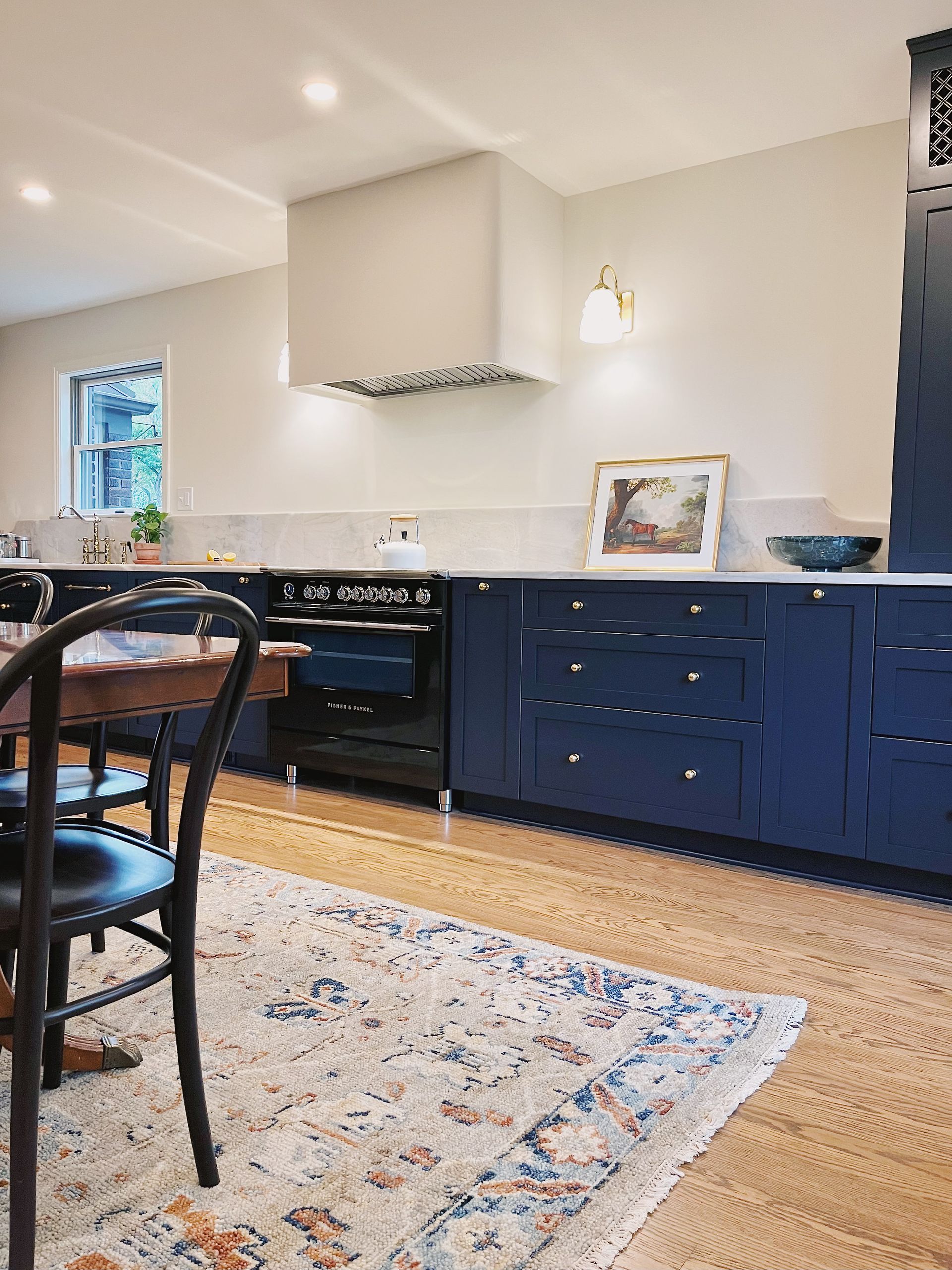 Bright kitchen with navy cabinets, white walls, black chair, and patterned rug near a window