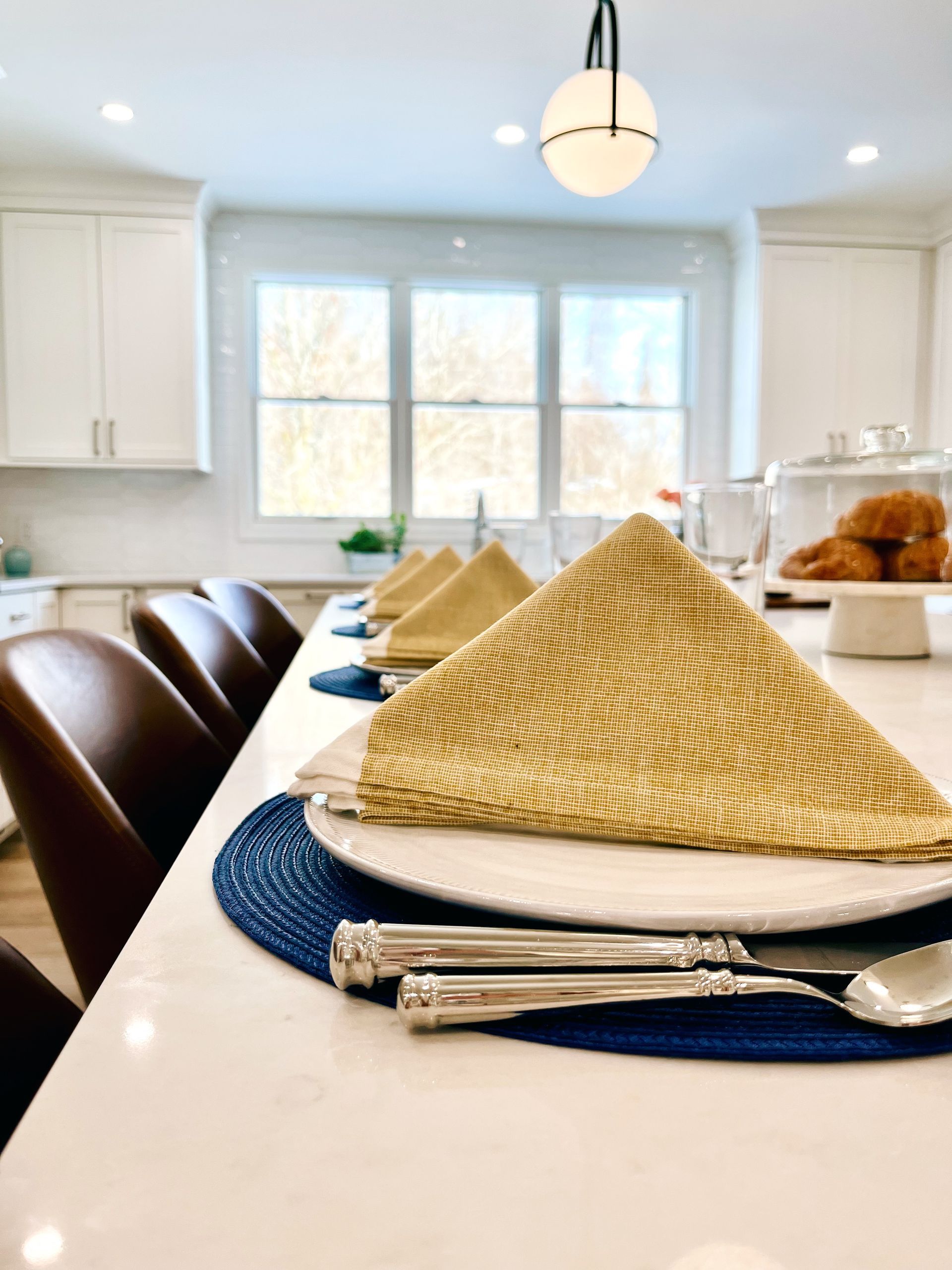 Modern kitchen island set with blue placemats, folded napkins, and white cabinets in the background
