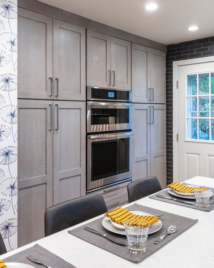 Modern kitchen with gray cabinets, built-in oven, white island, and set dining place settings near a window