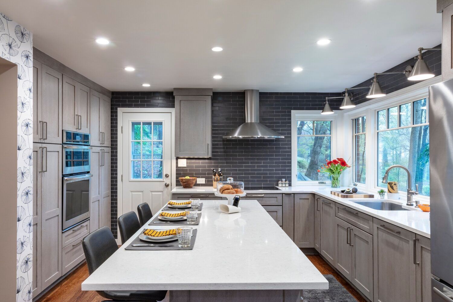 Modern kitchen with a large white island, gray cabinets, stainless appliances, and bright windows