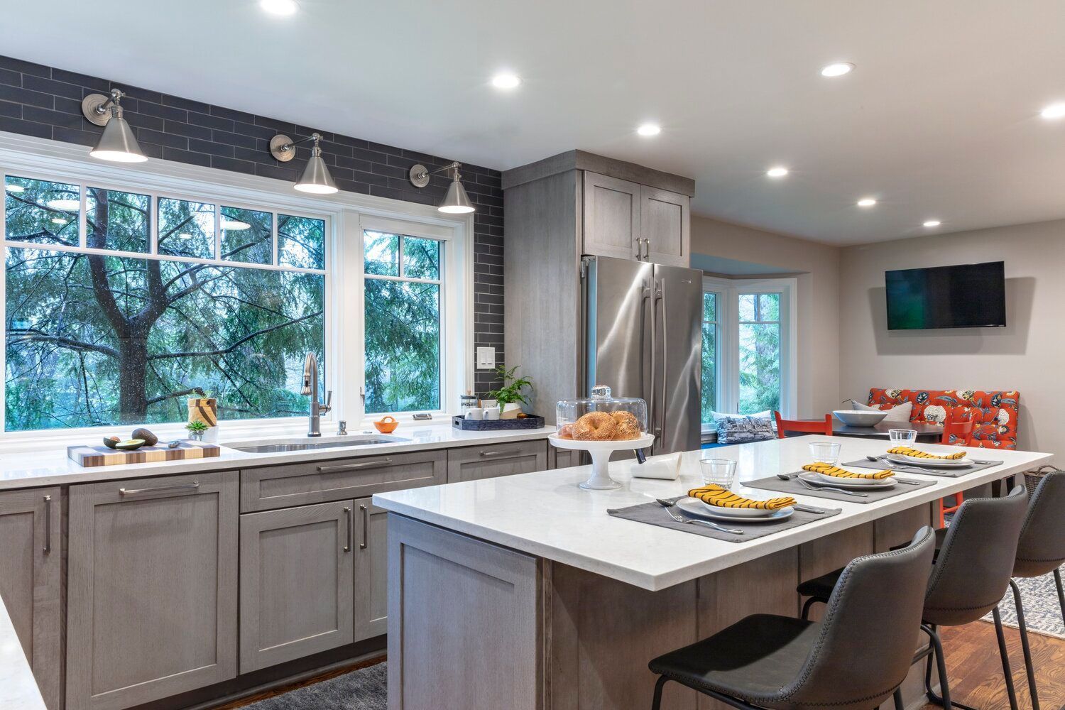 Modern kitchen with gray cabinets, large window, island seating, and a dining area with colorful chairs.