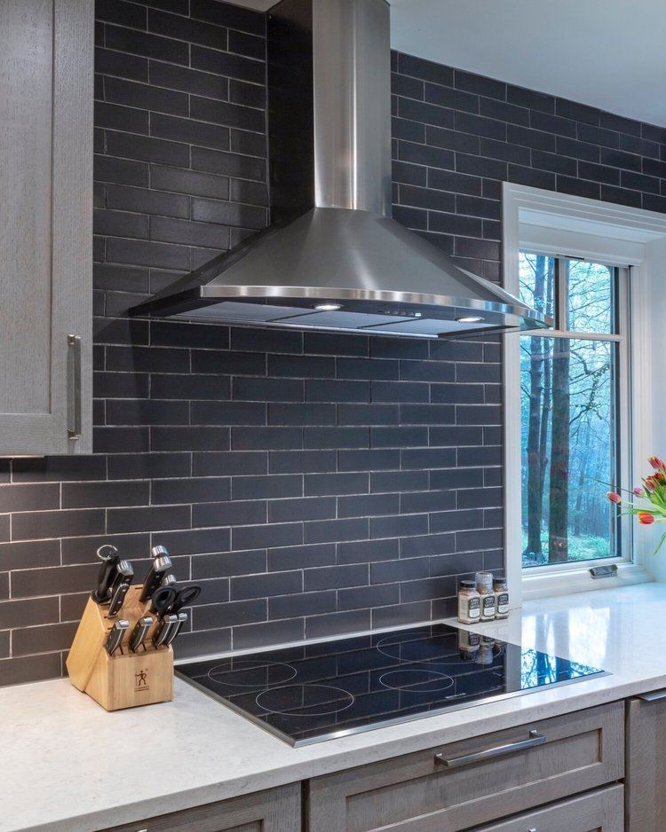 Modern kitchen with stainless range hood, black tile backsplash, white countertop, and window