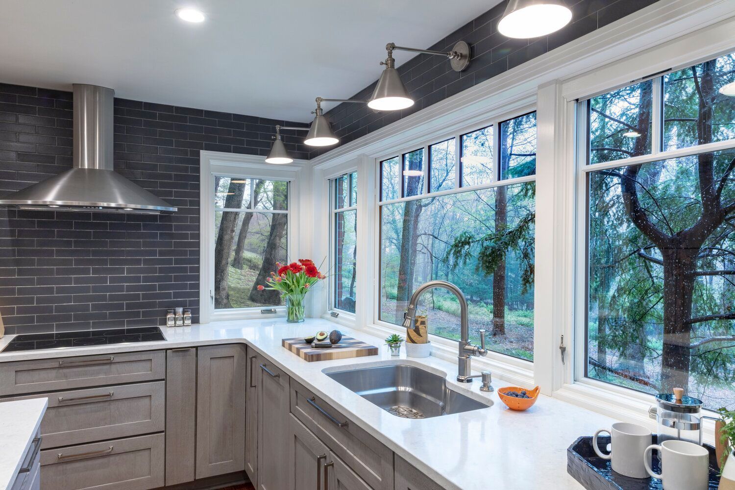 Modern kitchen with gray cabinets, black tile backsplash, white counters, and large windows overlooking trees