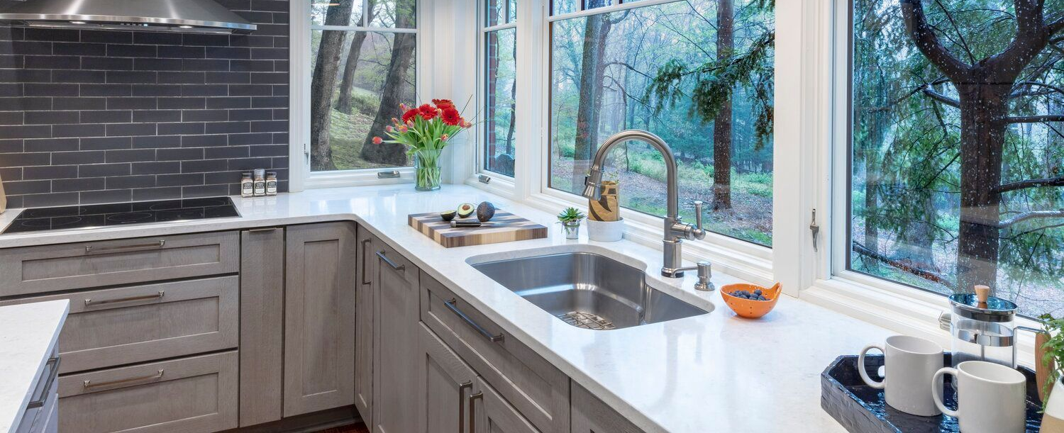 Modern kitchen with gray cabinets, white countertops, and a large window above the sink.