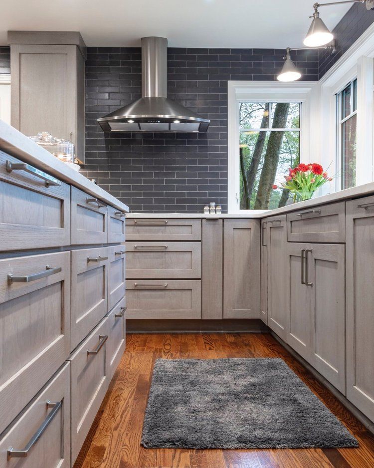 Modern gray kitchen with black backsplash, stainless range hood, wood floor, and a window with flowers