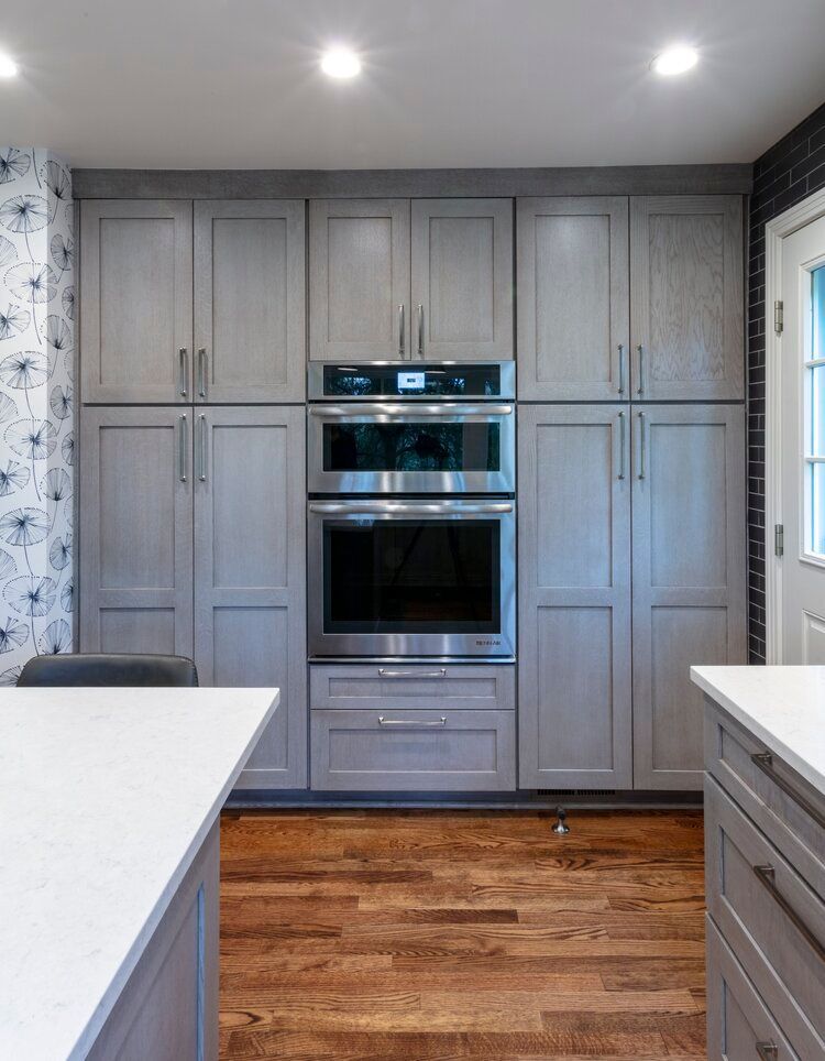 Modern kitchen with gray cabinets, built-in double oven, white countertops, and hardwood floor
