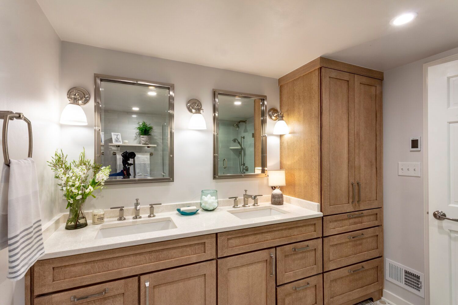 Bright bathroom vanity with double sinks, mirrors, wall sconces, and light wood cabinetry