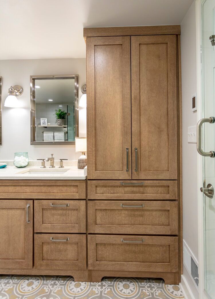 Wood bathroom vanity with double sink, mirror, and tall cabinet in a tiled room
