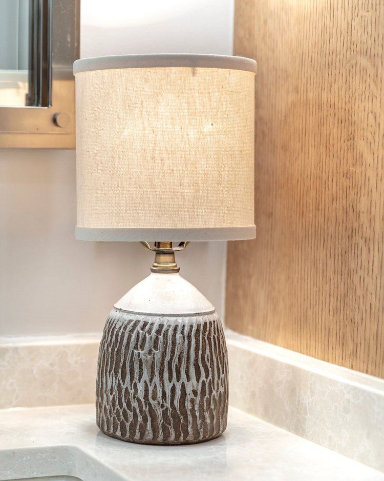 Ceramic table lamp with beige shade on a bathroom counter beside a wall mirror