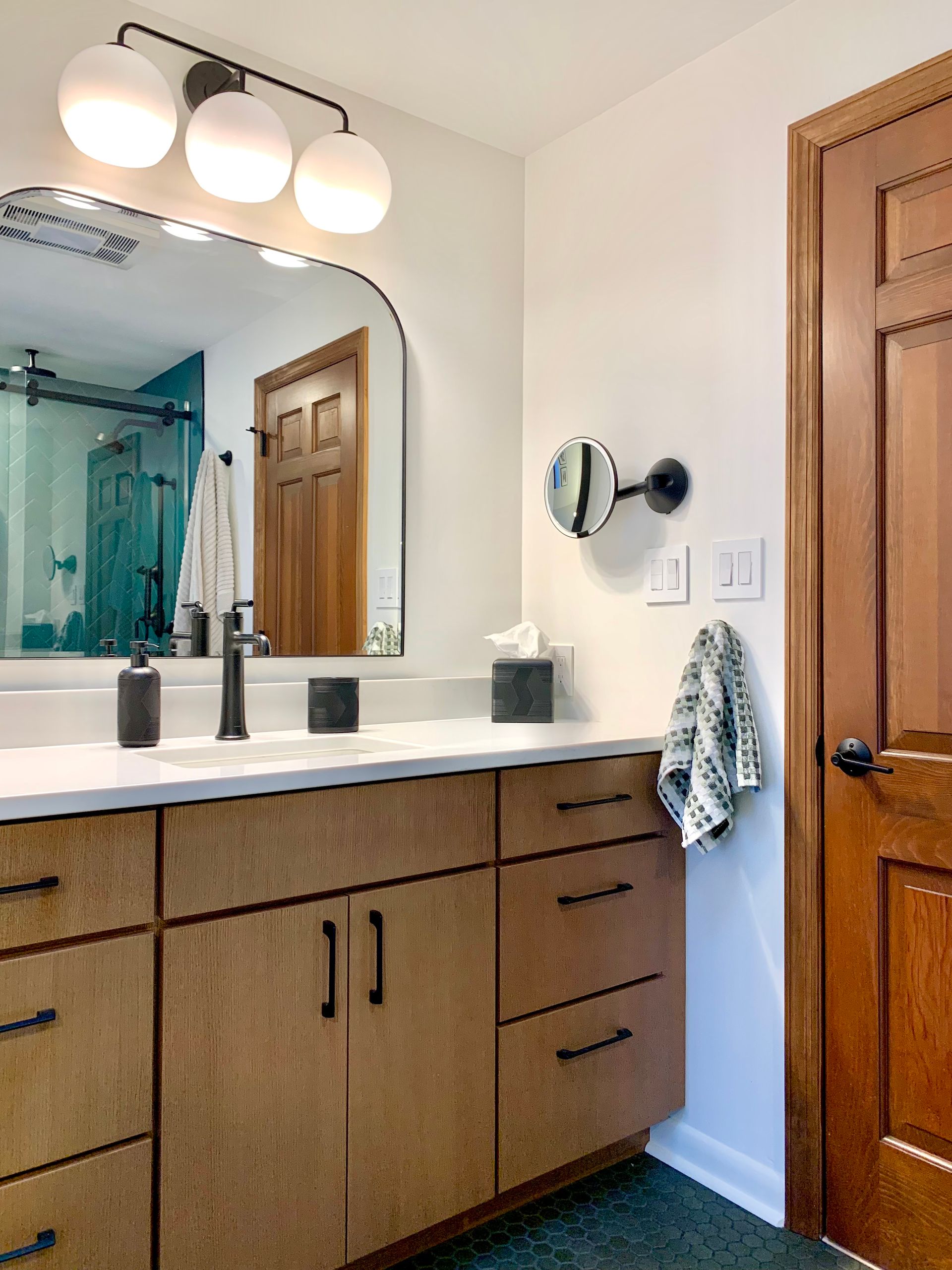 Modern bathroom vanity with double sinks, wood cabinets, mirror, and shower in the background
