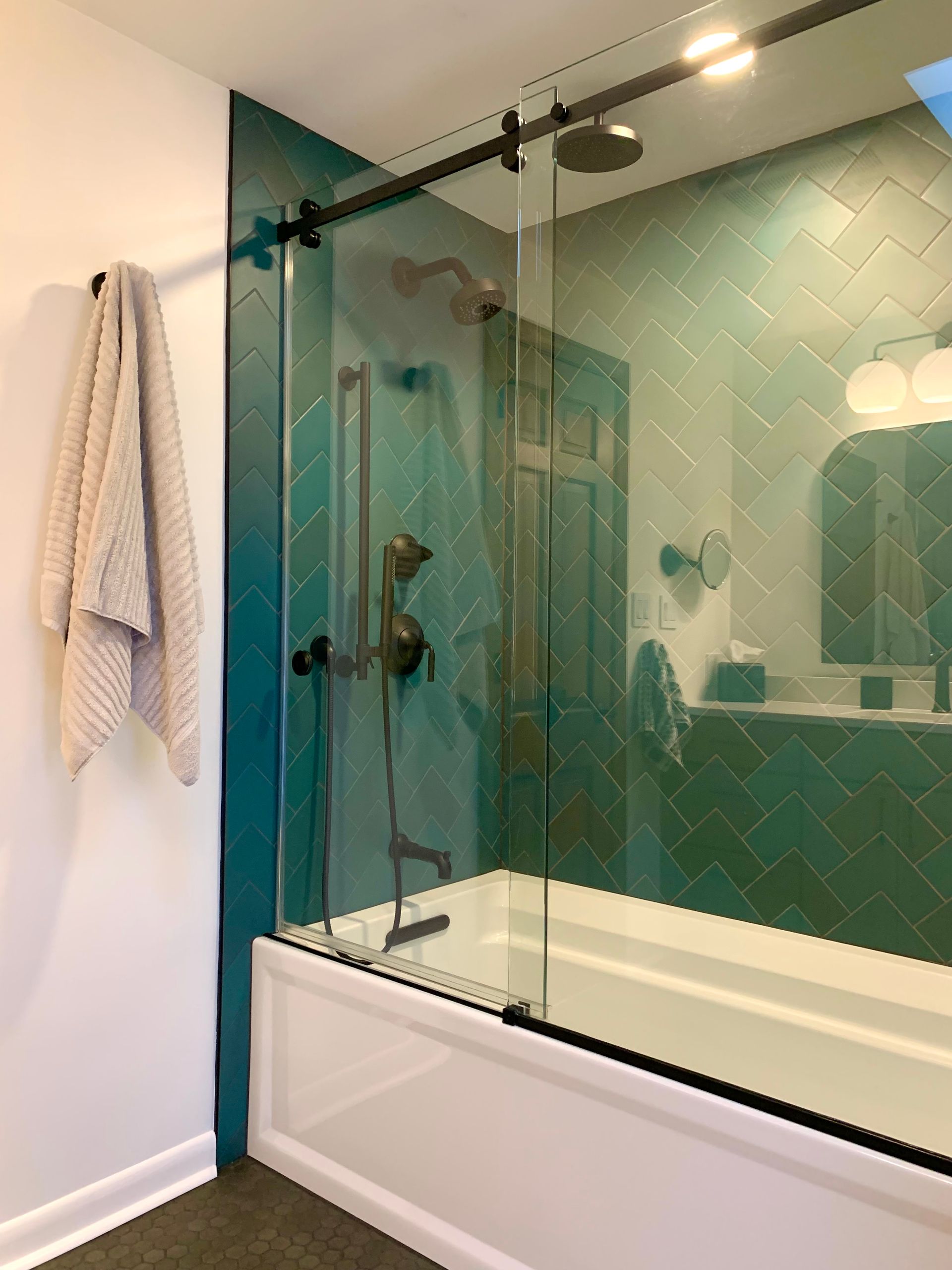 Bathroom with glass shower enclosure, white tub, and teal tile wall.