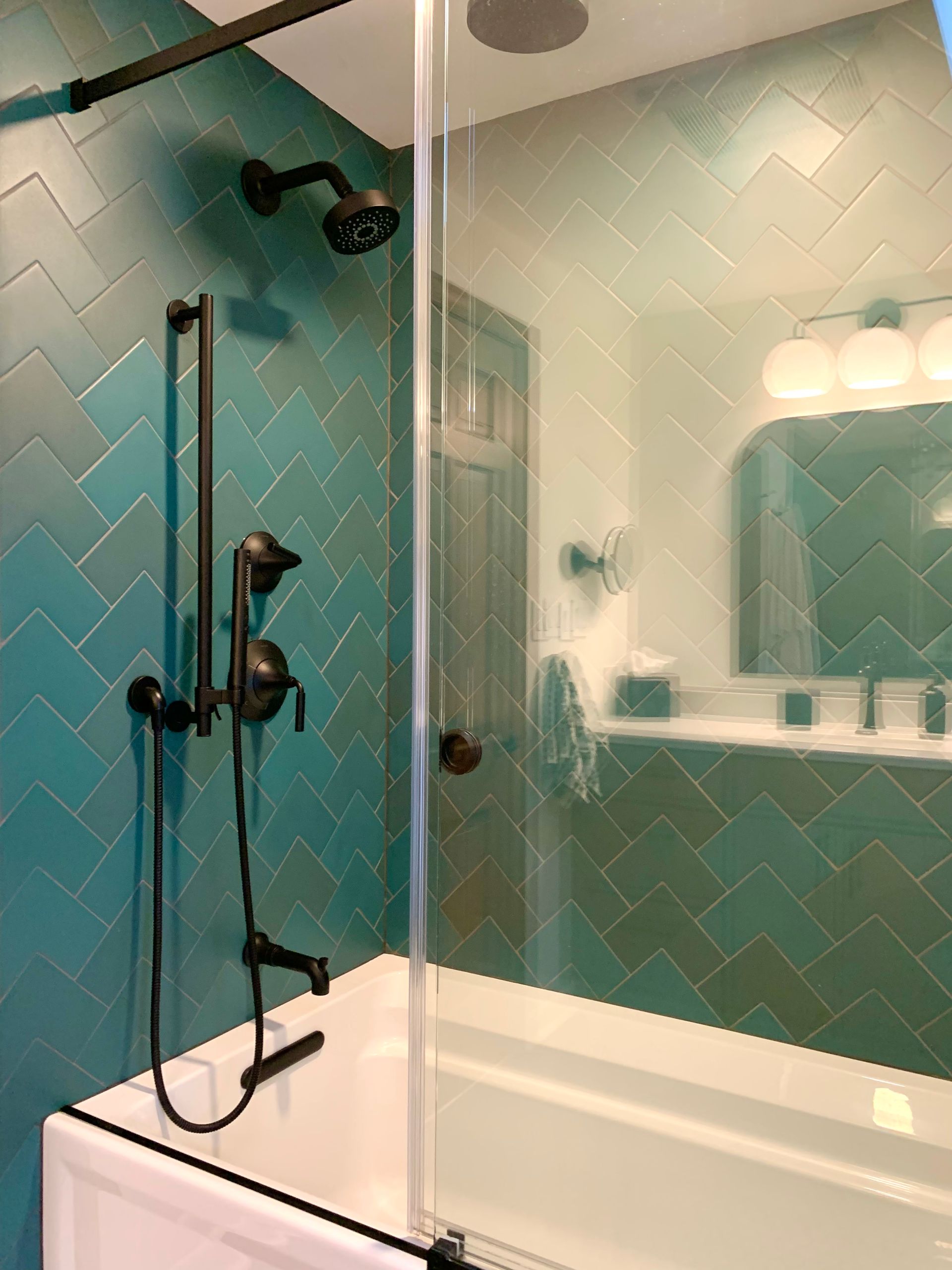 Modern bathroom with turquoise tile, glass shower doors, and a white vanity mirror with lights