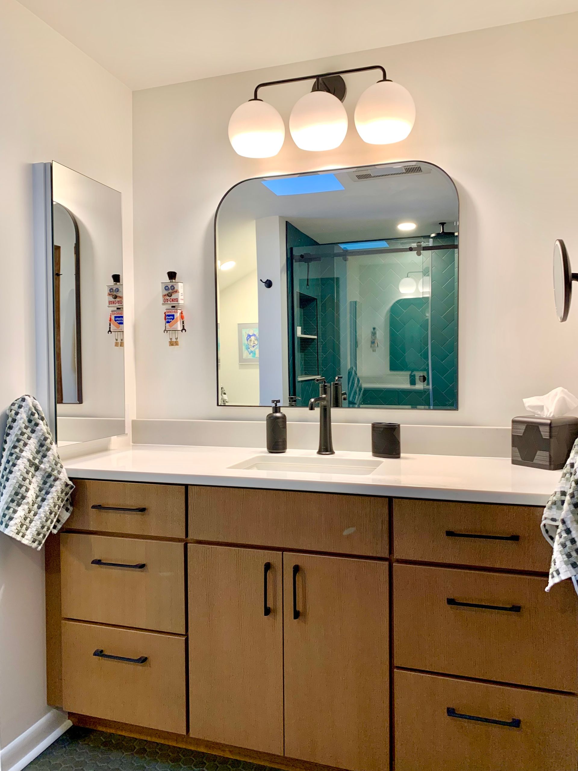 Bathroom vanity with double sinks, wood cabinets, and a large arched mirror under three globe lights.