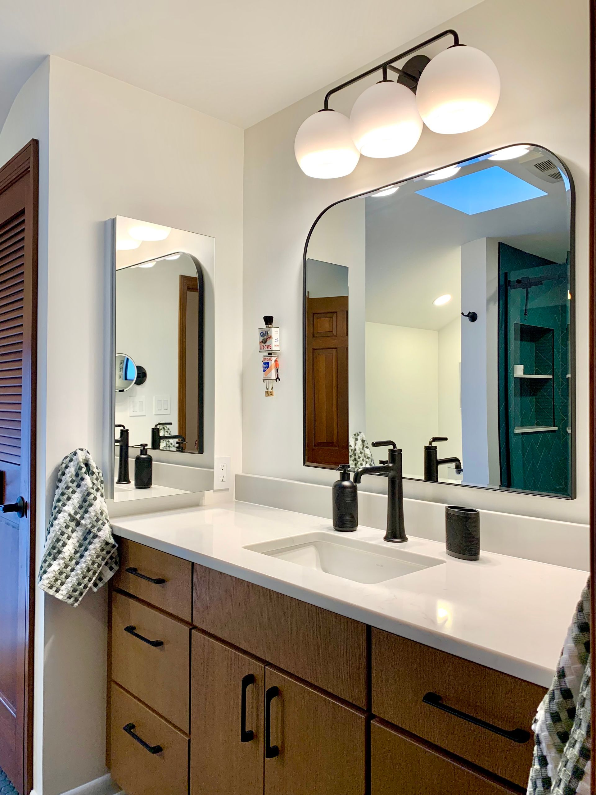 Modern bathroom vanity with two mirrors, white countertop, wood cabinets, and black fixtures