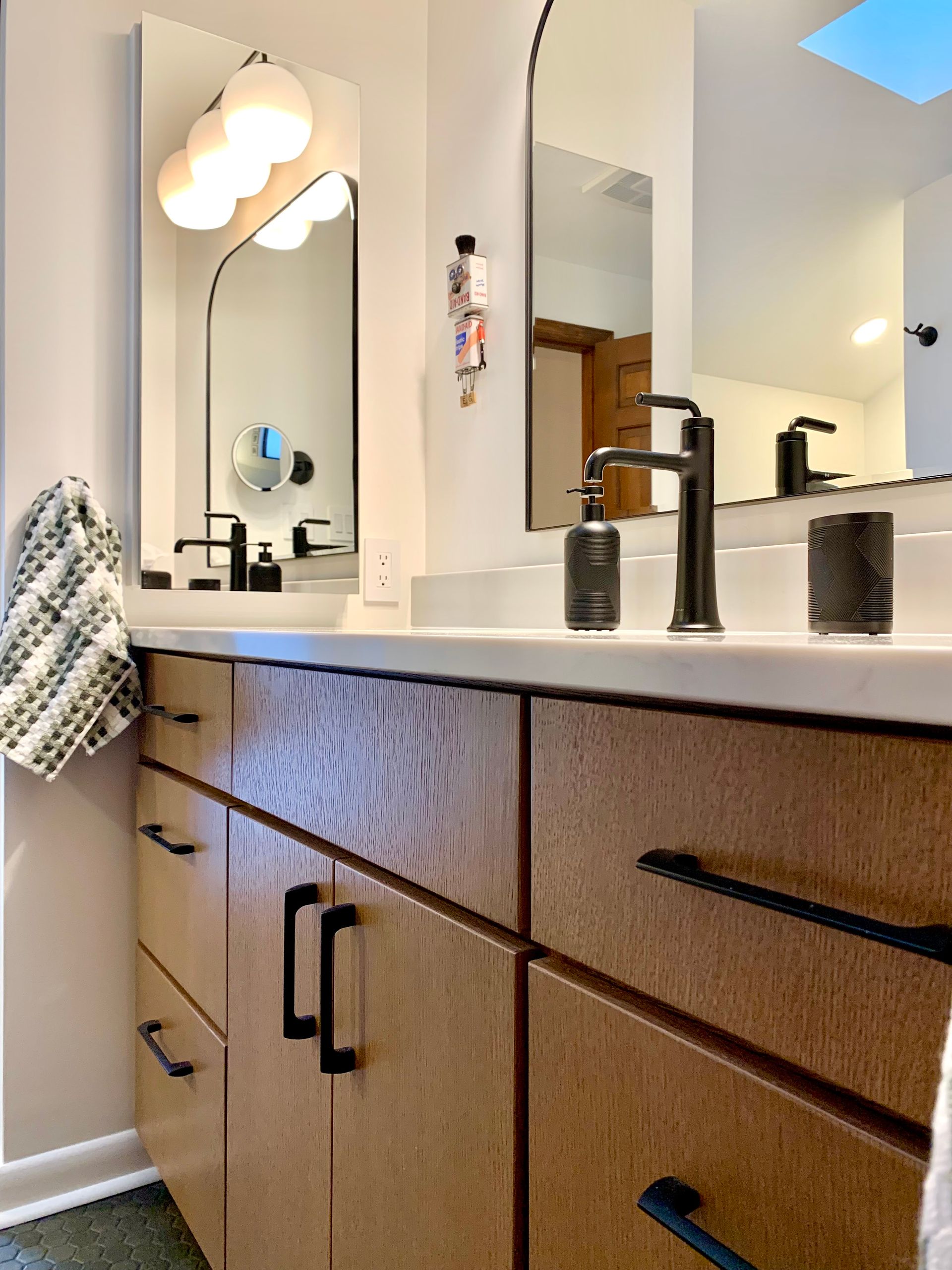 Modern bathroom vanity with wood cabinets, white countertop, black fixtures, and wall mirrors