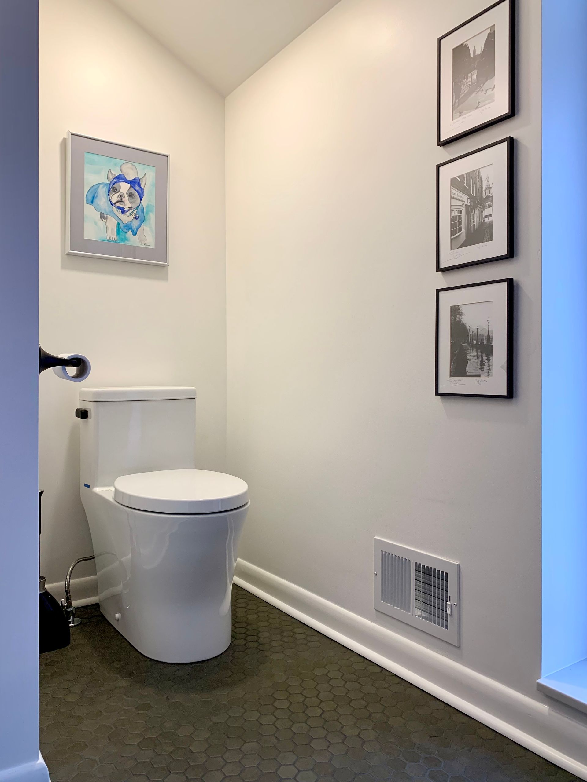 Small bathroom with a modern toilet, framed wall art, and a vent on the wall.