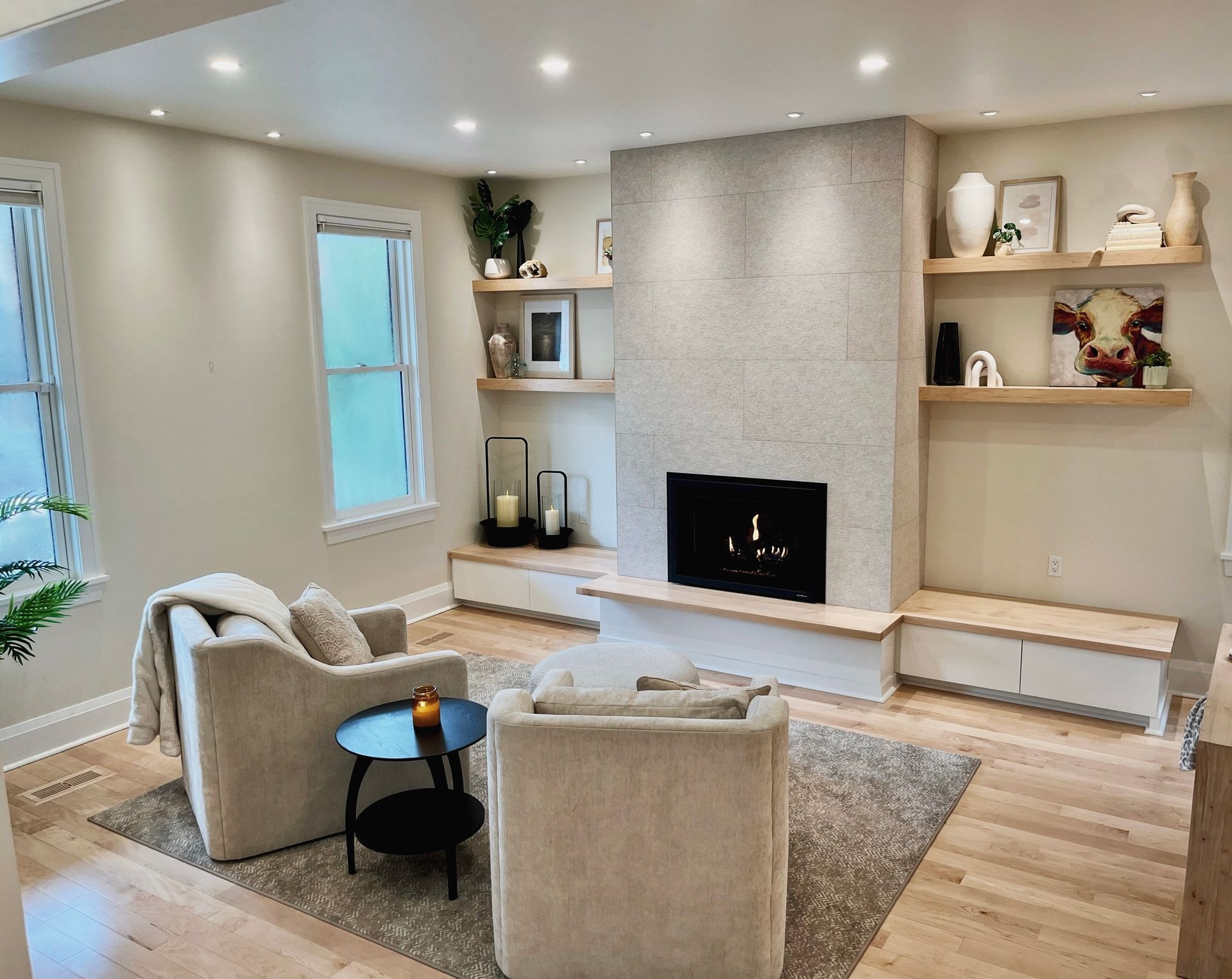 Bright living room with beige chairs, gray fireplace wall, open shelves, and soft natural light
