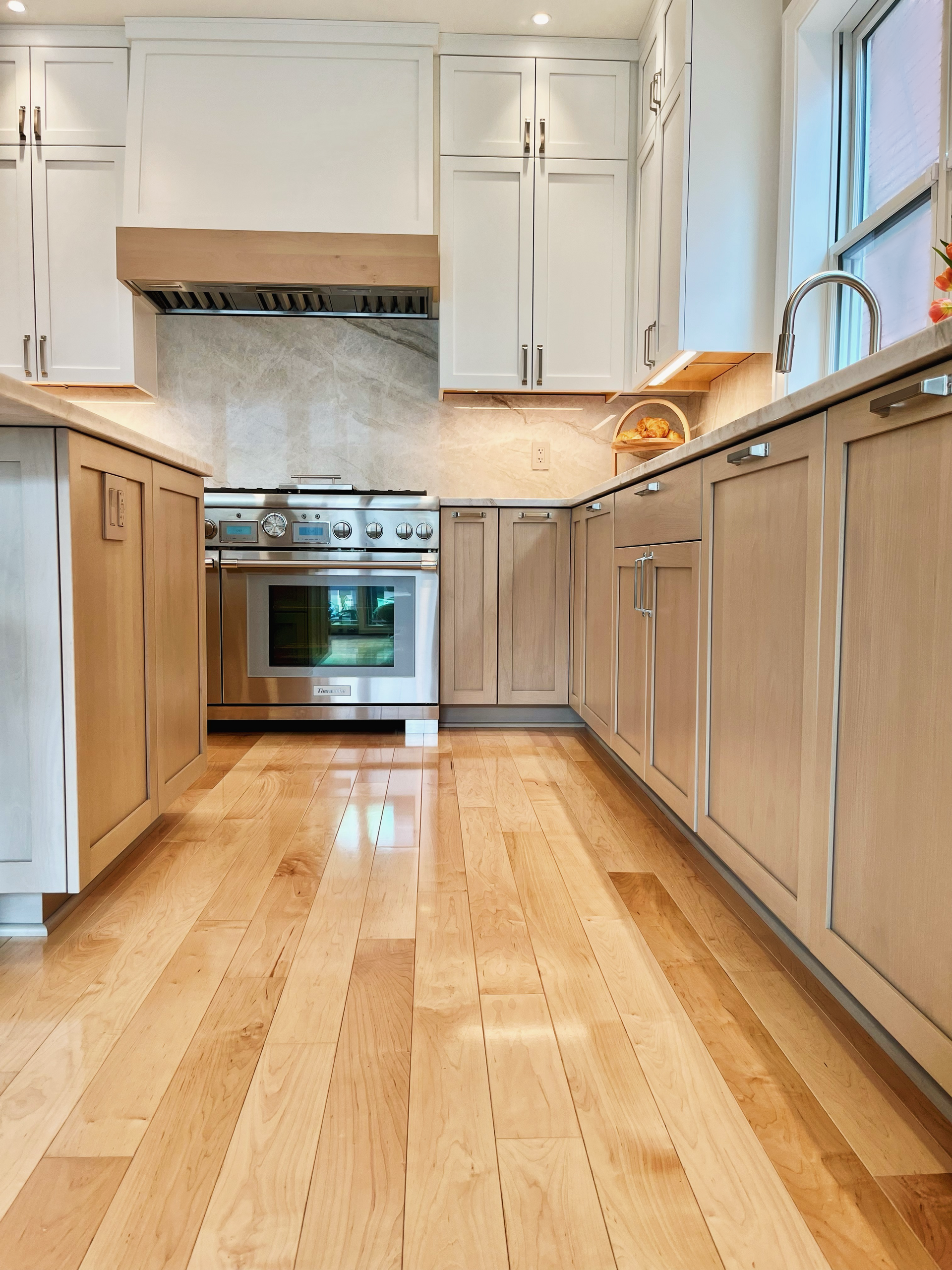 Bright modern kitchen with white cabinets, wood flooring, stainless steel stove, and a large window.