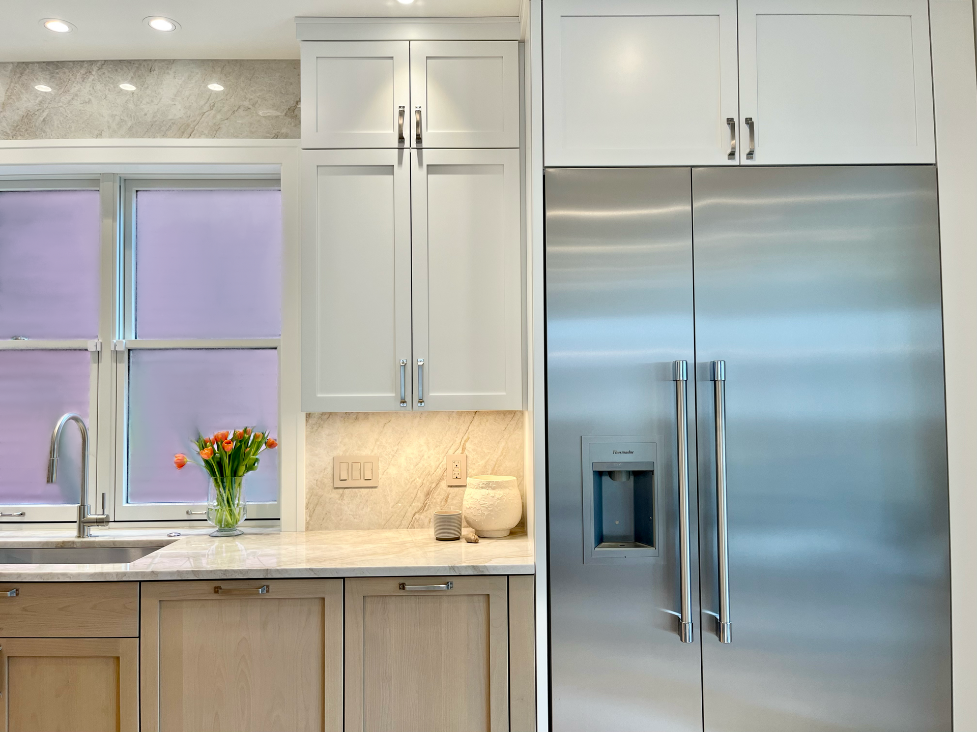 Modern kitchen with white cabinets, stainless steel refrigerator, and a vase of flowers by the window