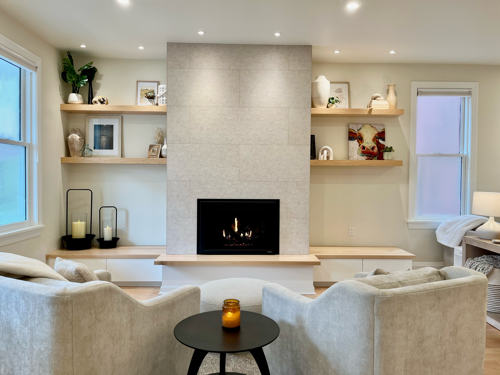 Modern living room with stone fireplace, built-in shelves, and two beige armchairs facing a small table.