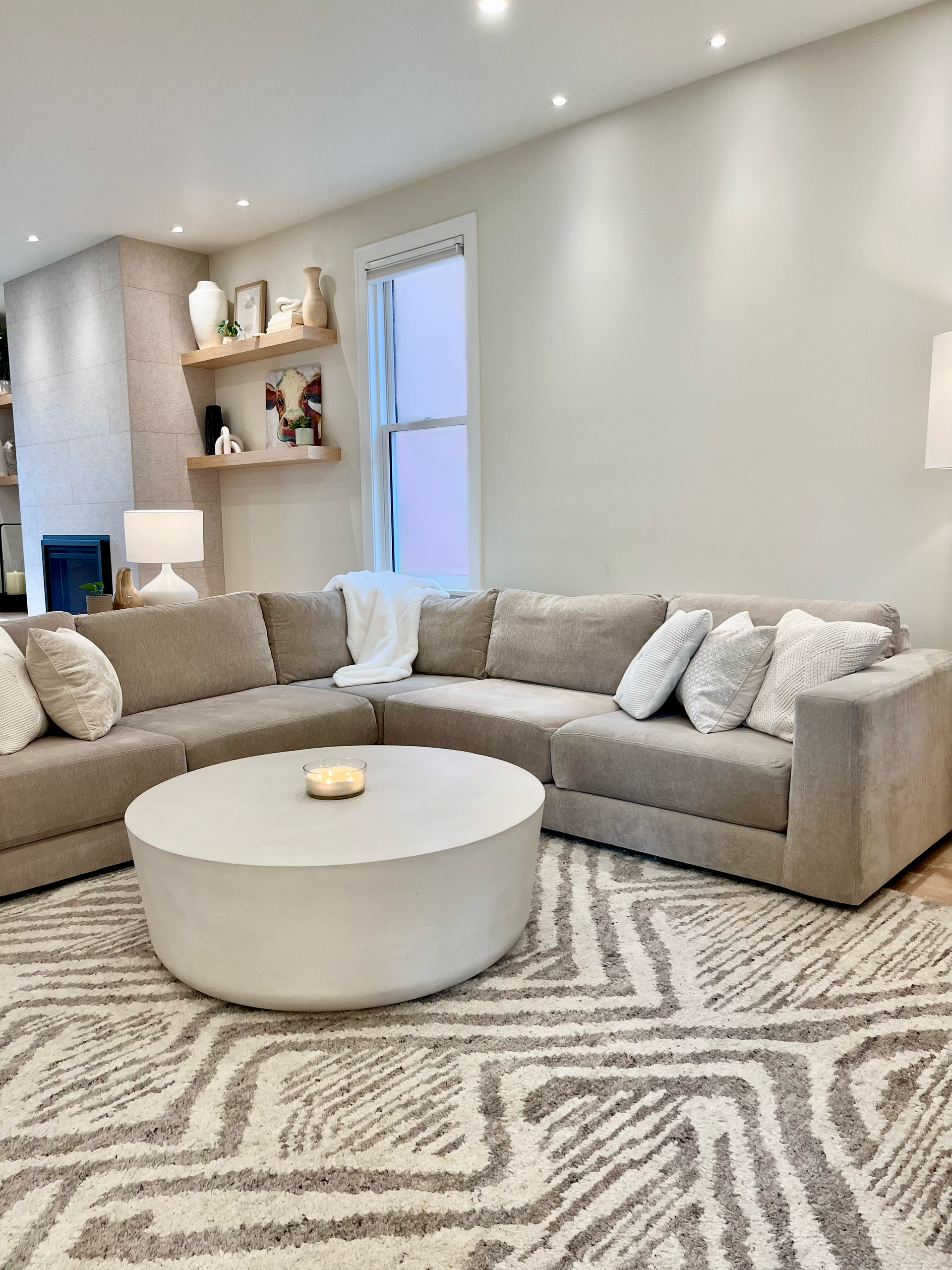 Modern living room with a beige sectional, round white coffee table, patterned rug, and recessed lighting