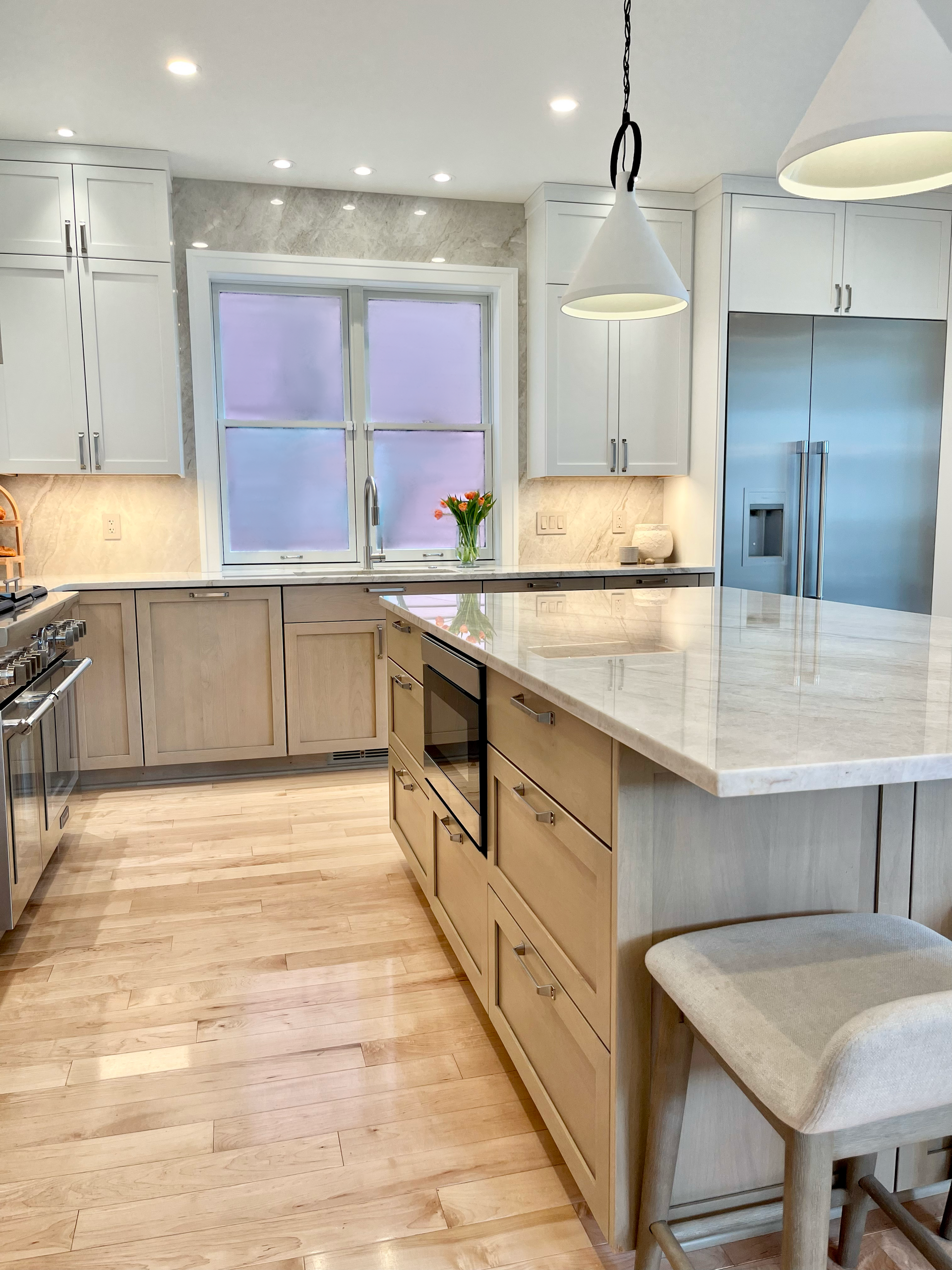 Bright modern kitchen with marble island, white cabinets, pendant lights, and a window over the sink.
