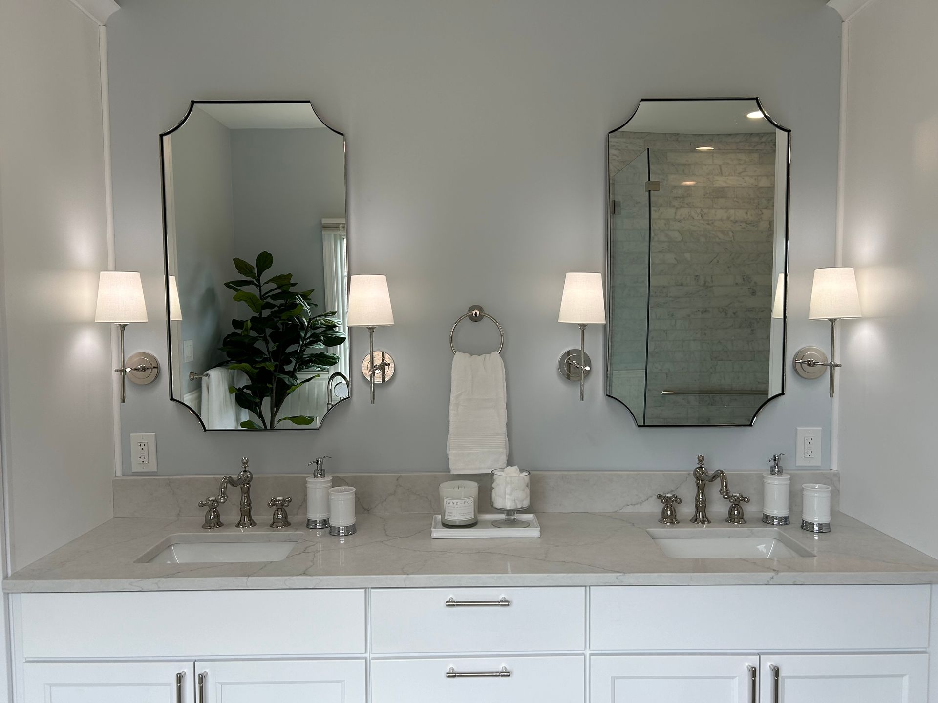 Elegant bathroom vanity with twin mirrors, wall sconces, and white countertop decor
