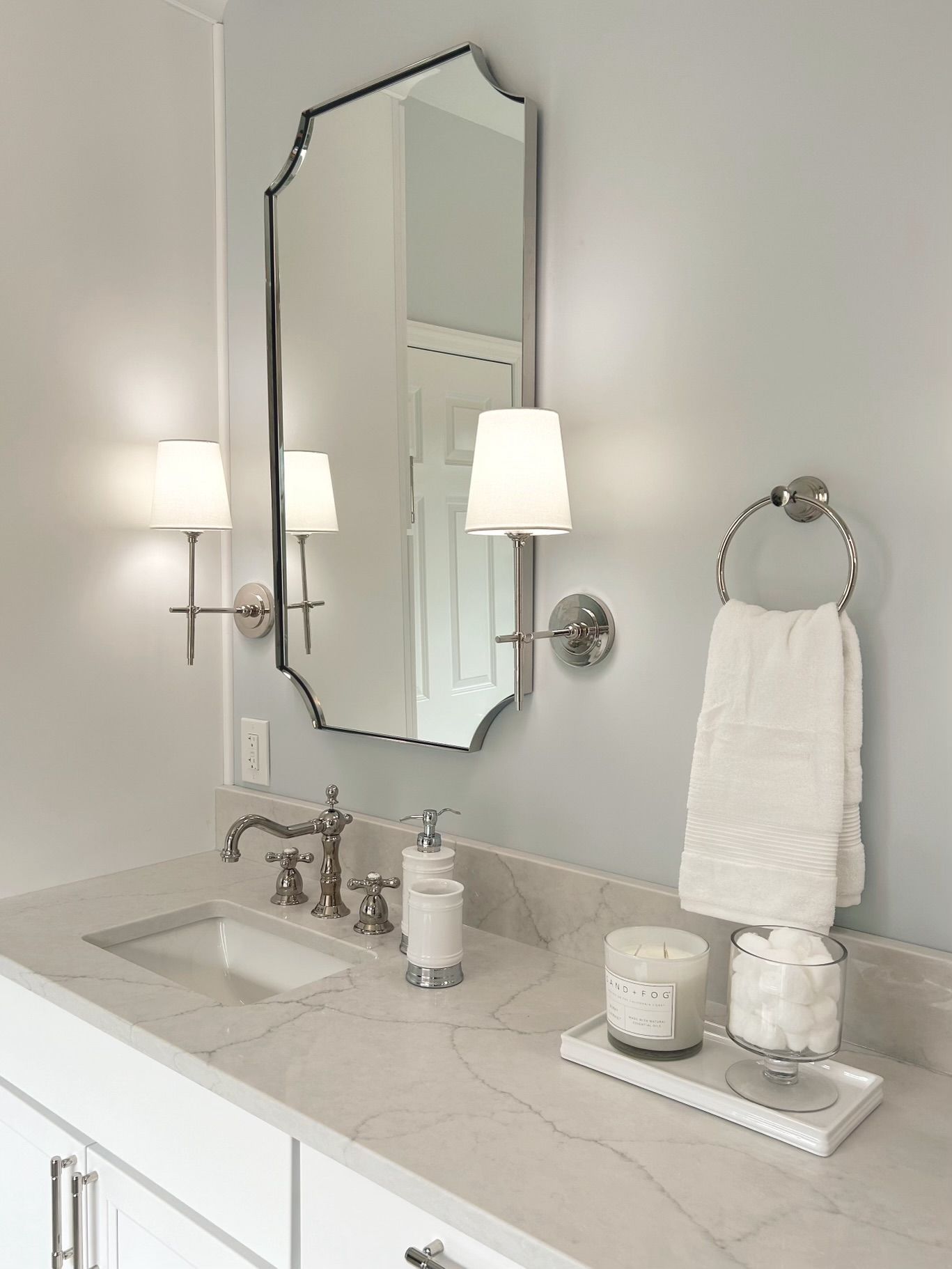 Bright bathroom vanity with mirror, wall sconces, white towels, and soap on a marble countertop.