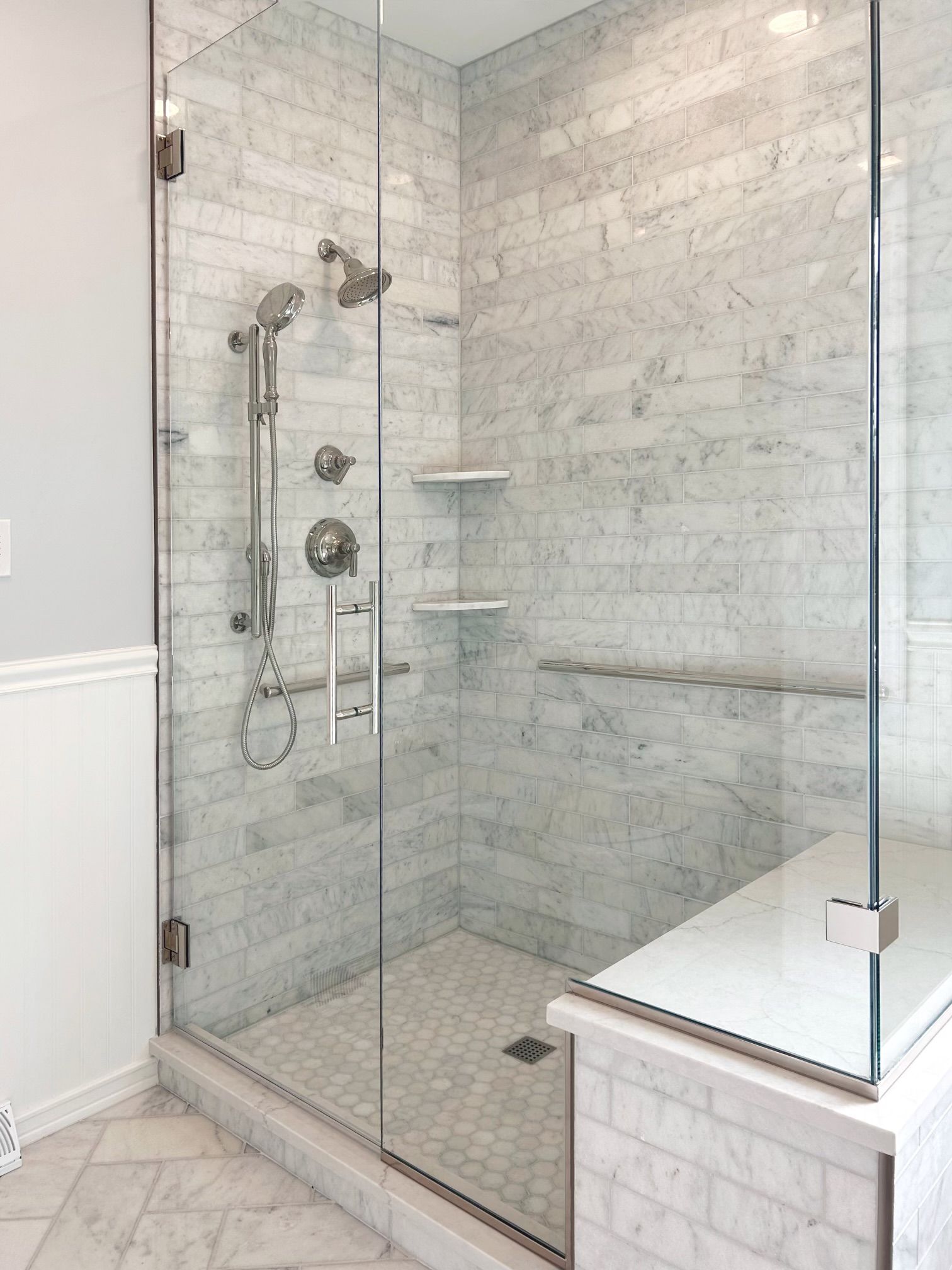 Modern glass walk-in shower with marble tile, chrome fixtures, and built-in corner shelves.
