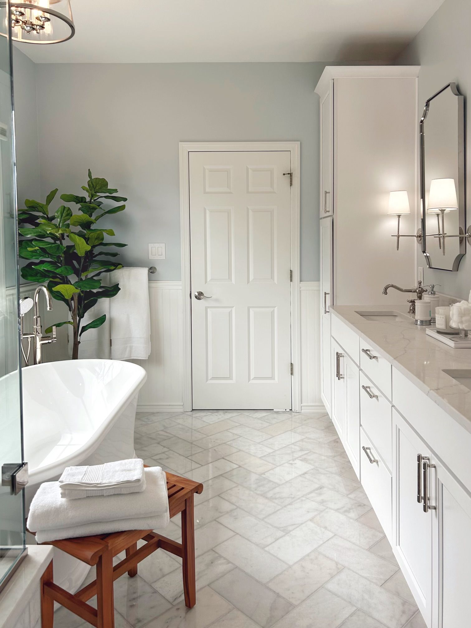 Modern bathroom with white vanity, freestanding tub, and herringbone tile floor.