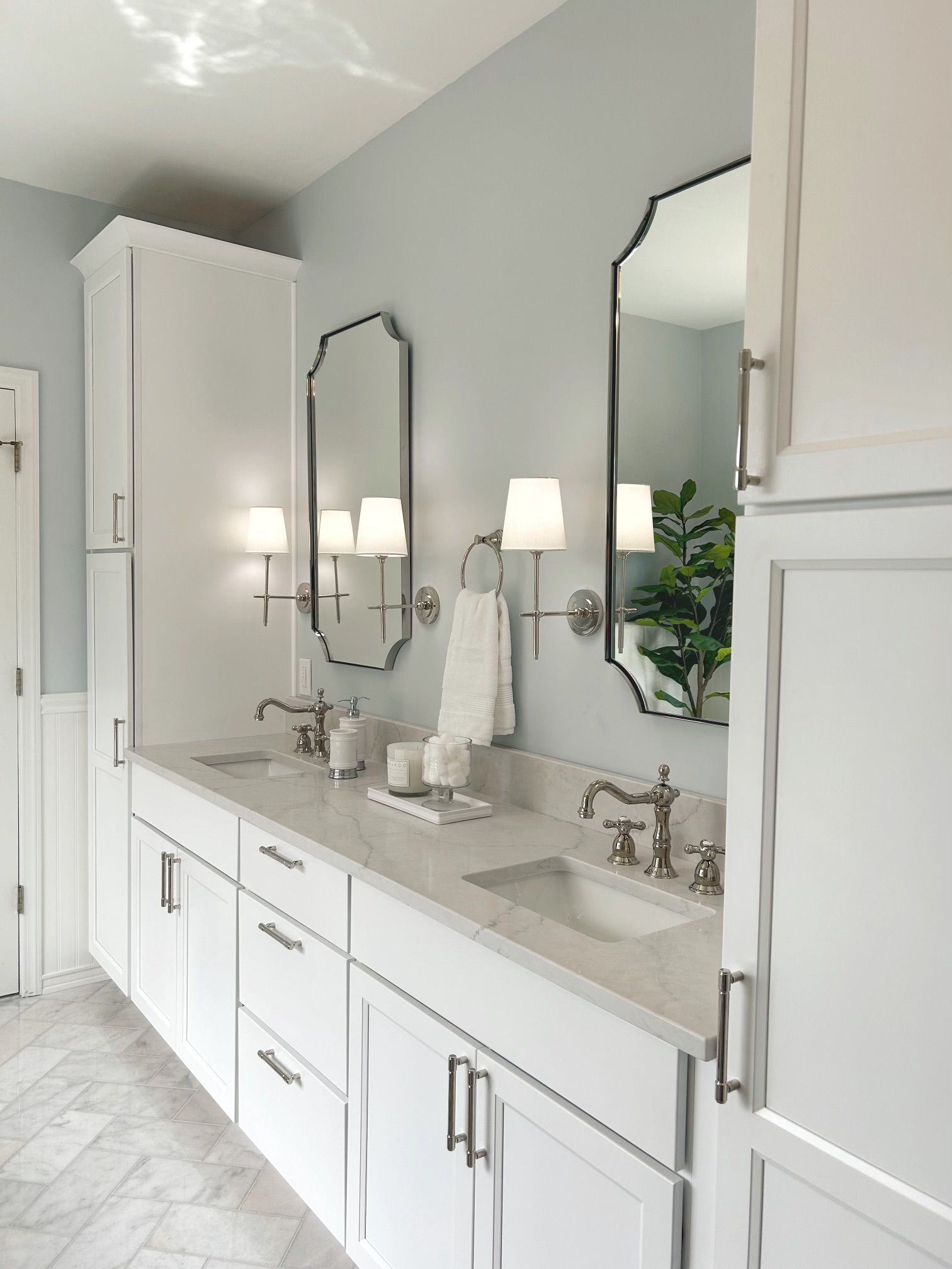 Bright white bathroom vanity with double sinks, mirrors, sconces, and cabinets in a light gray room