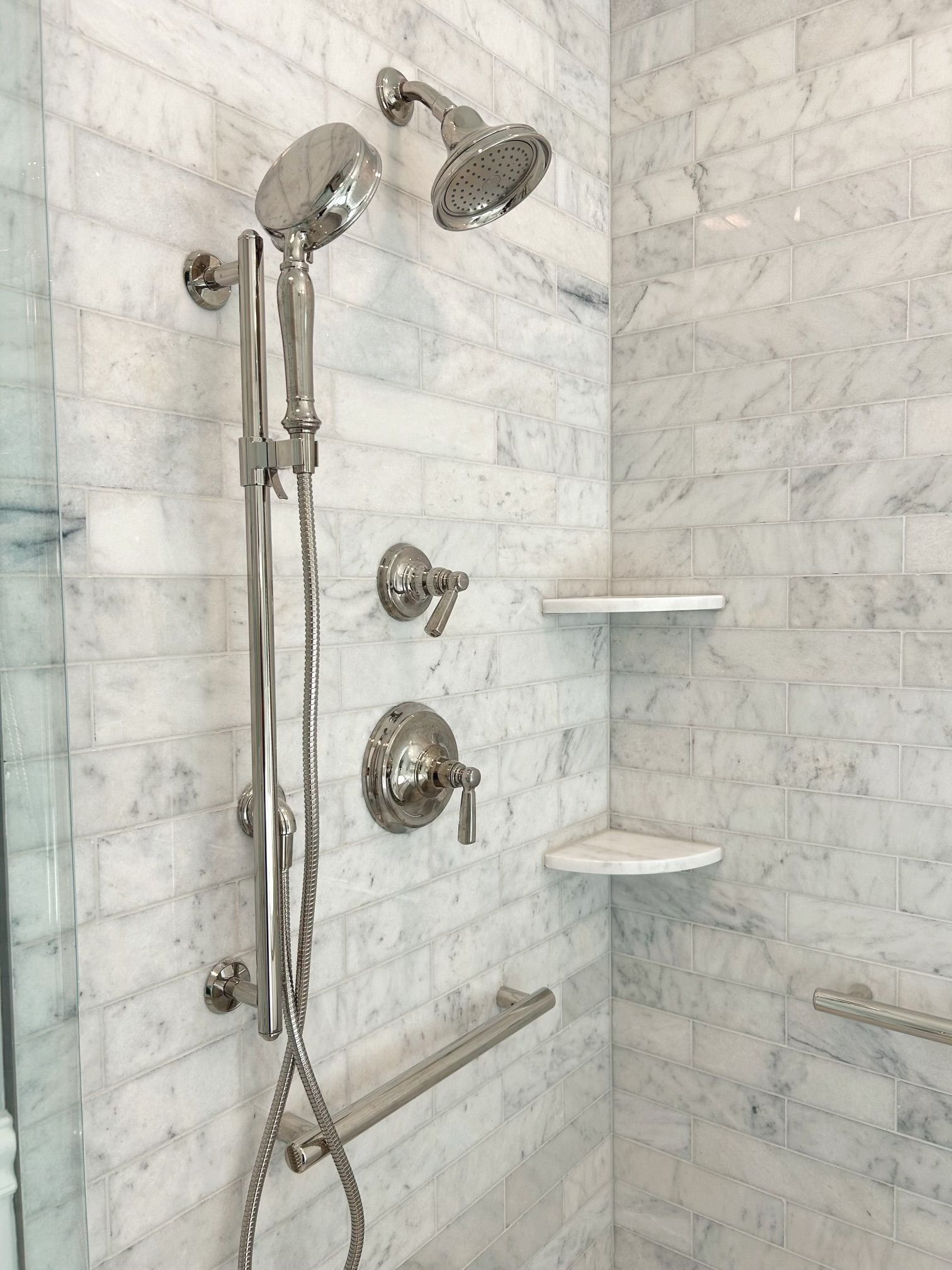 Modern tiled shower with chrome showerhead, handheld sprayer, and two corner shelves