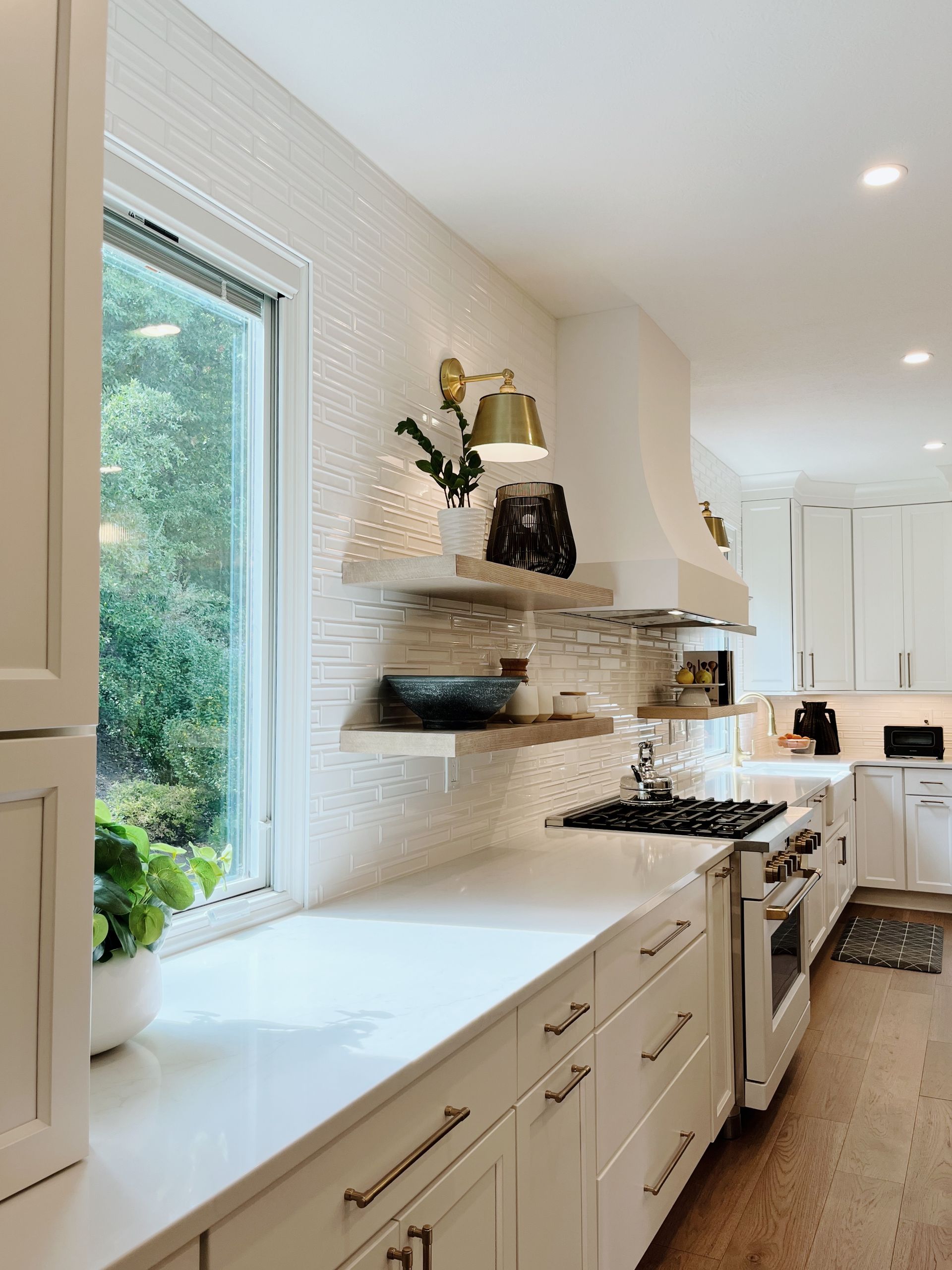 Bright white kitchen with long window seat, open shelves, and a gas stove along the right wall.