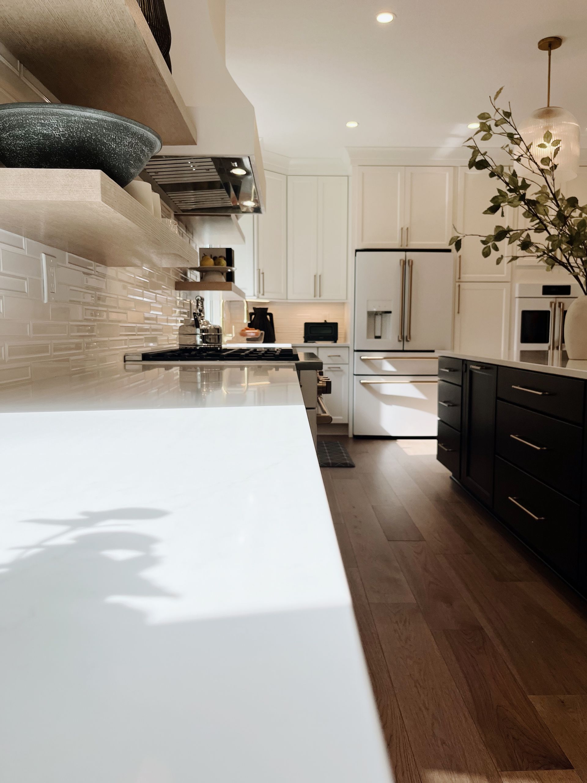 Bright modern kitchen with white counters, dark cabinets, wood floors, and a stainless steel refrigerator.