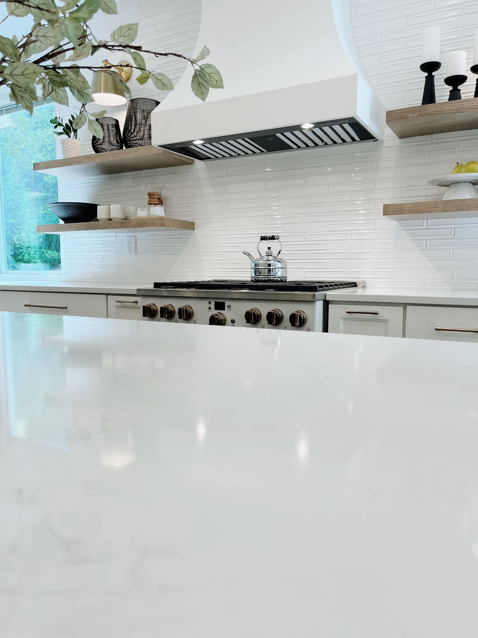 Bright modern kitchen with white countertops, shelves, black range hood, and stainless-steel stove