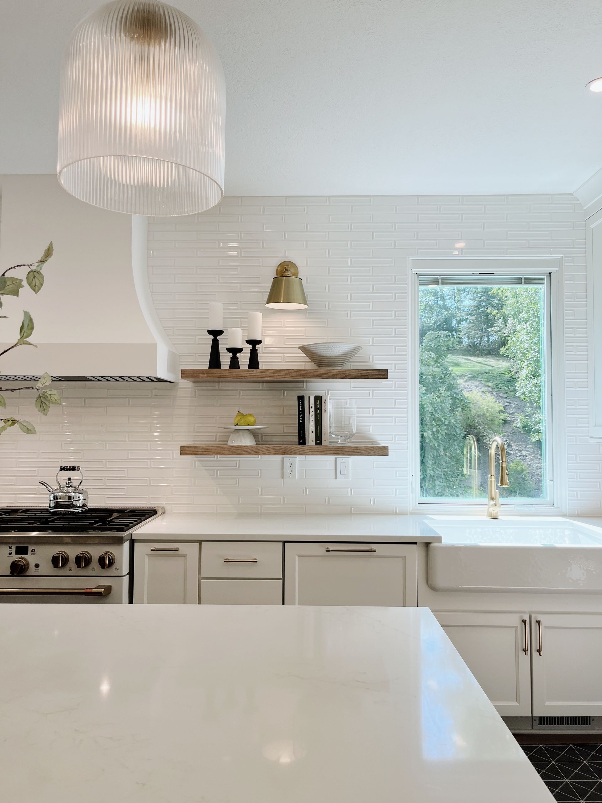 Bright white kitchen with stove, open shelves, and a window overlooking greenery
