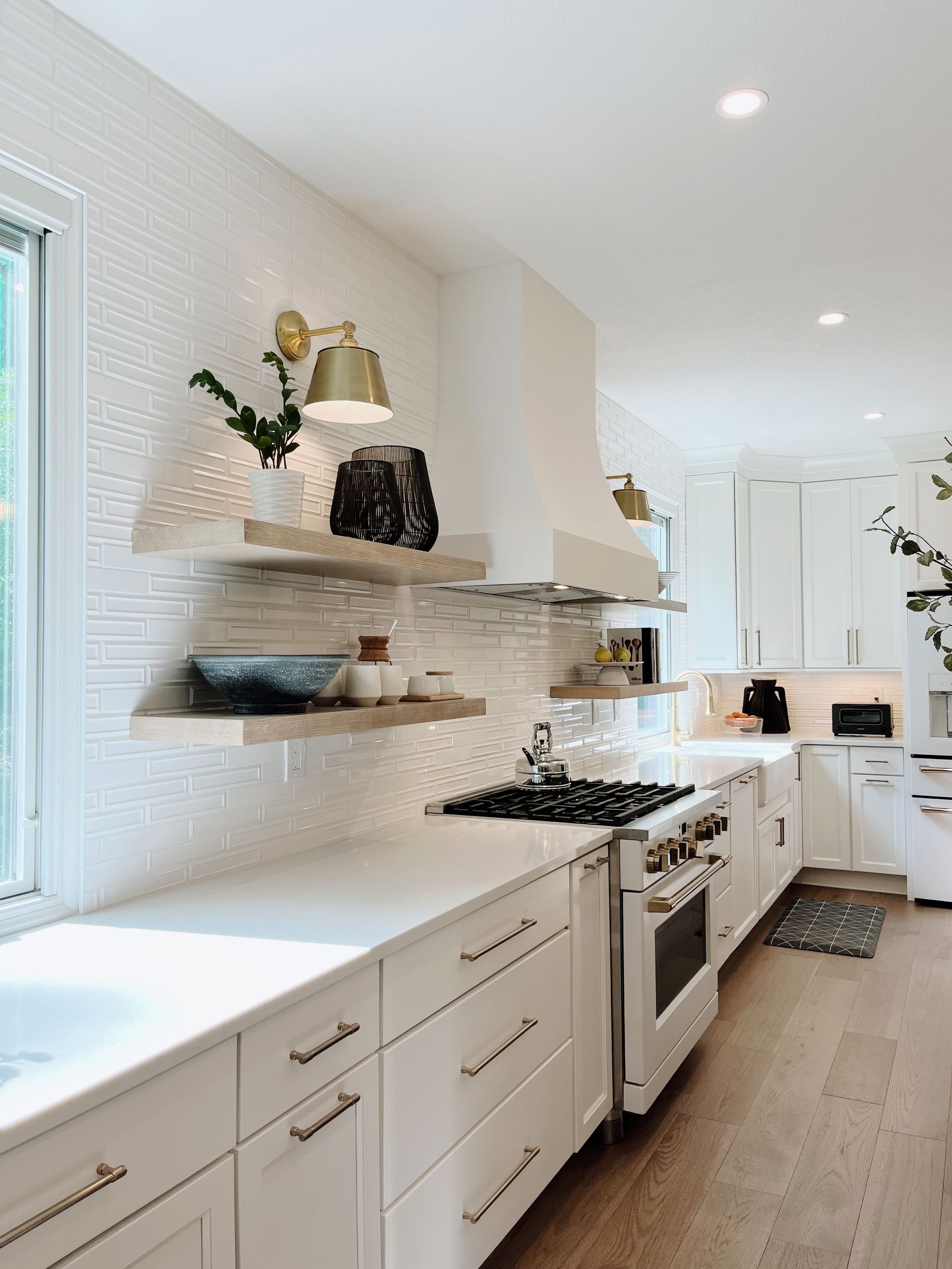 Bright white kitchen with open shelves, long counters, and a stainless stove in a narrow hallway layout