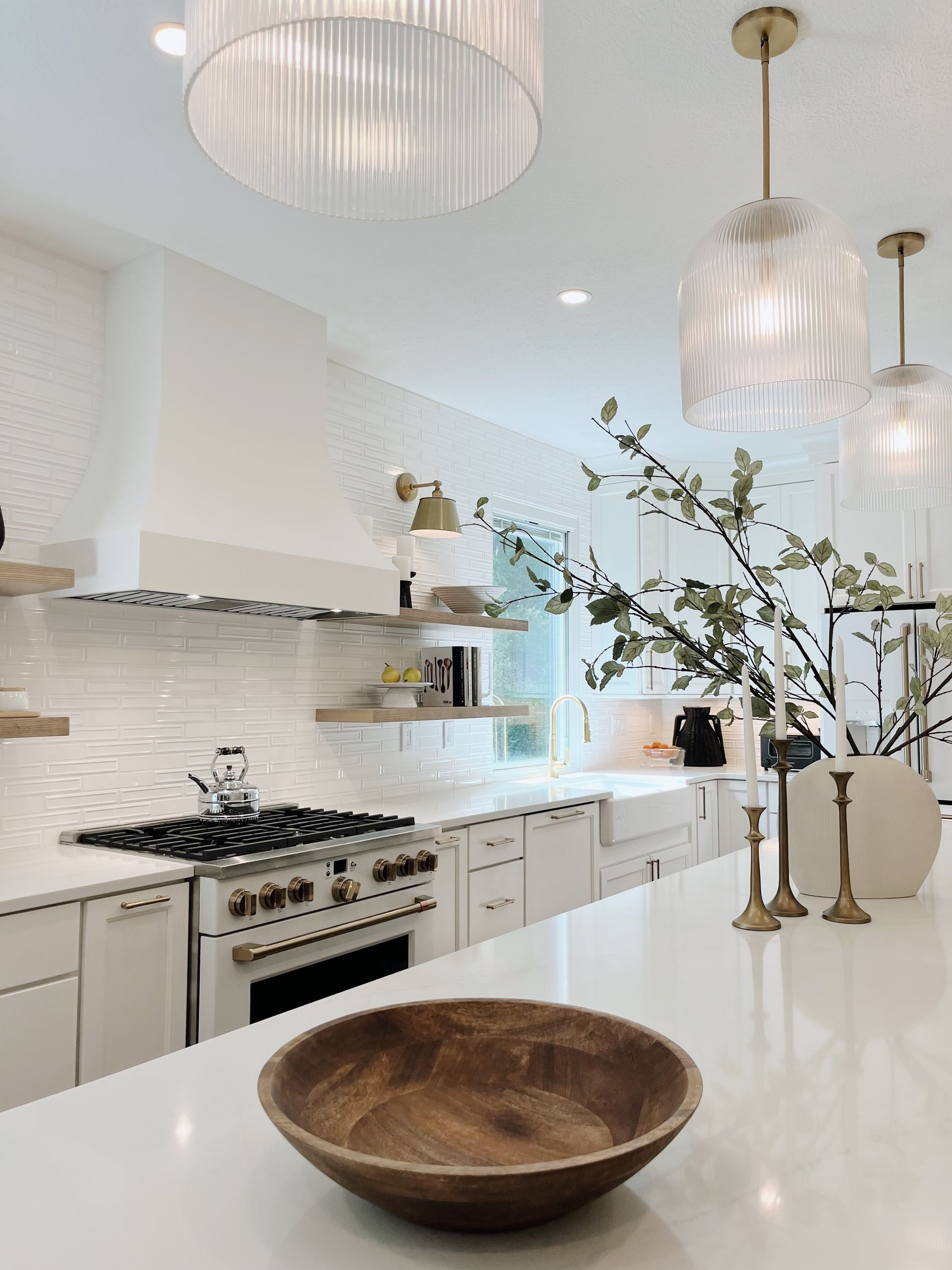 Bright white modern kitchen with marble island, wood bowl, and glass pendant lights