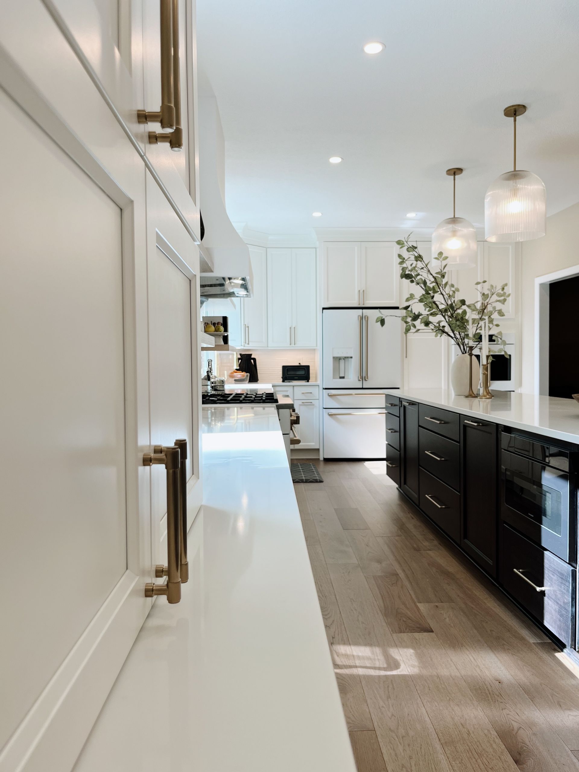 Bright modern kitchen with white cabinets, black lower cabinets, pendant lights, and a long island.