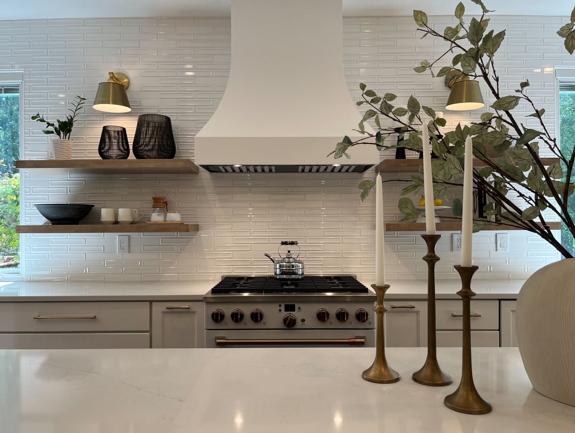 Bright white kitchen with marble island, gas range, shelves, and tall brass candlesticks in foreground