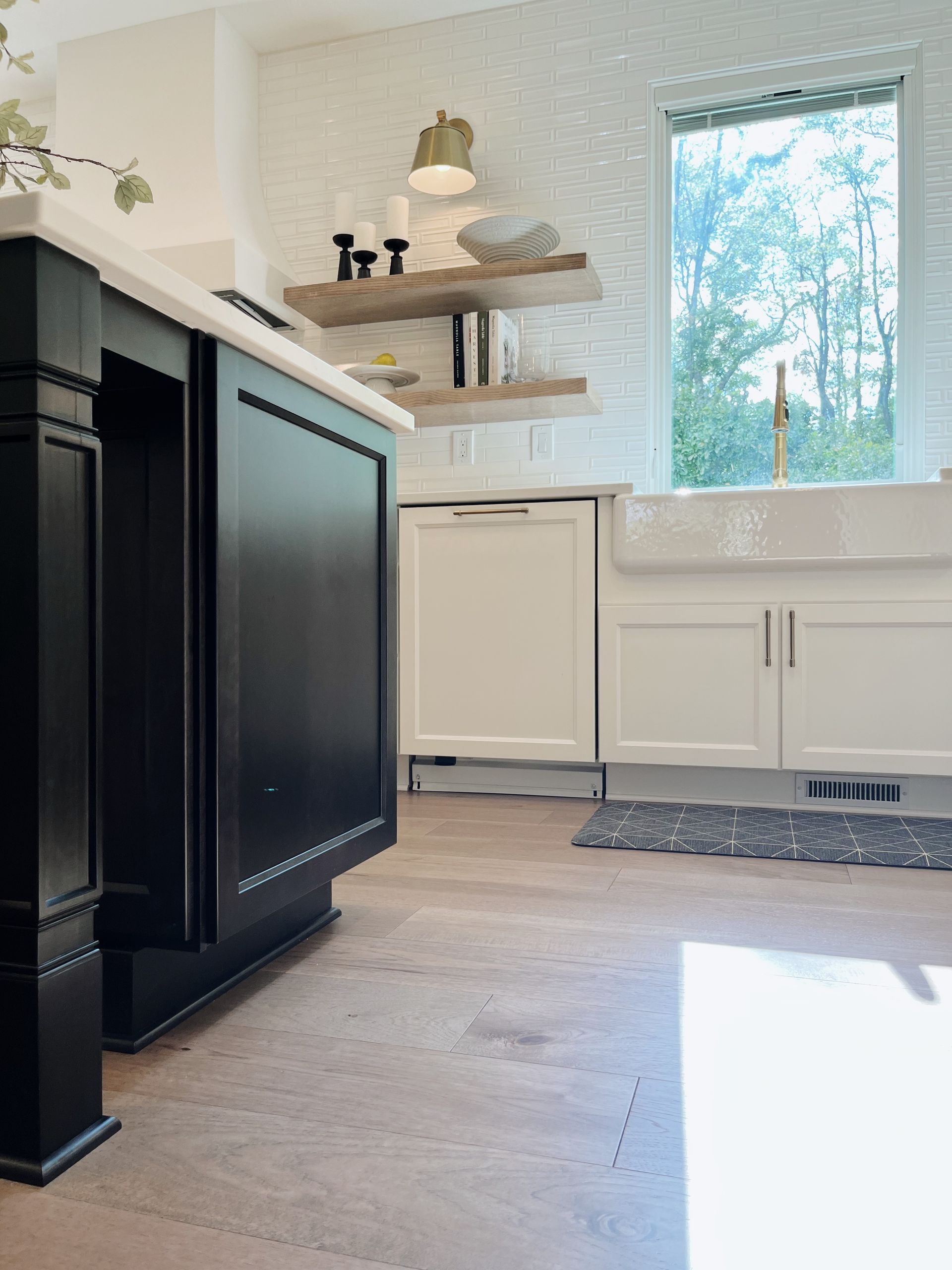 Bright kitchen with black island, white cabinets, open shelves, and sunlight by a window