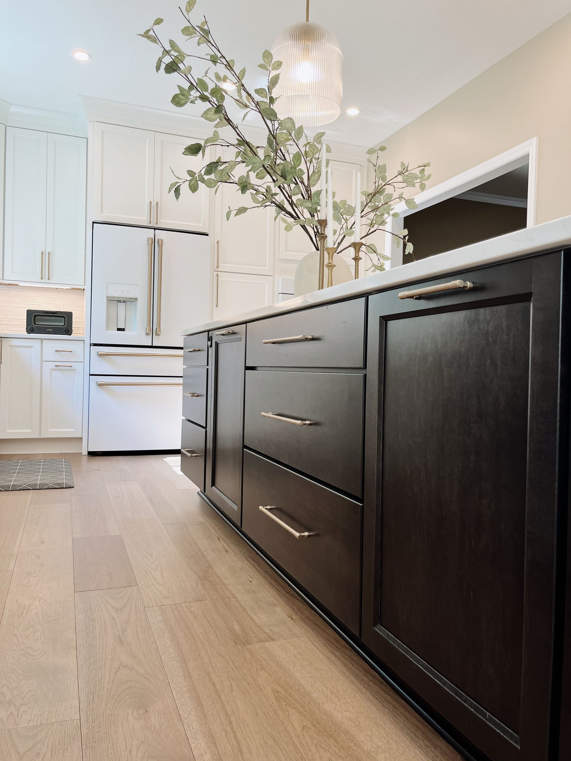 Modern white kitchen with dark wood island cabinets, light countertops, and a vase of branches.